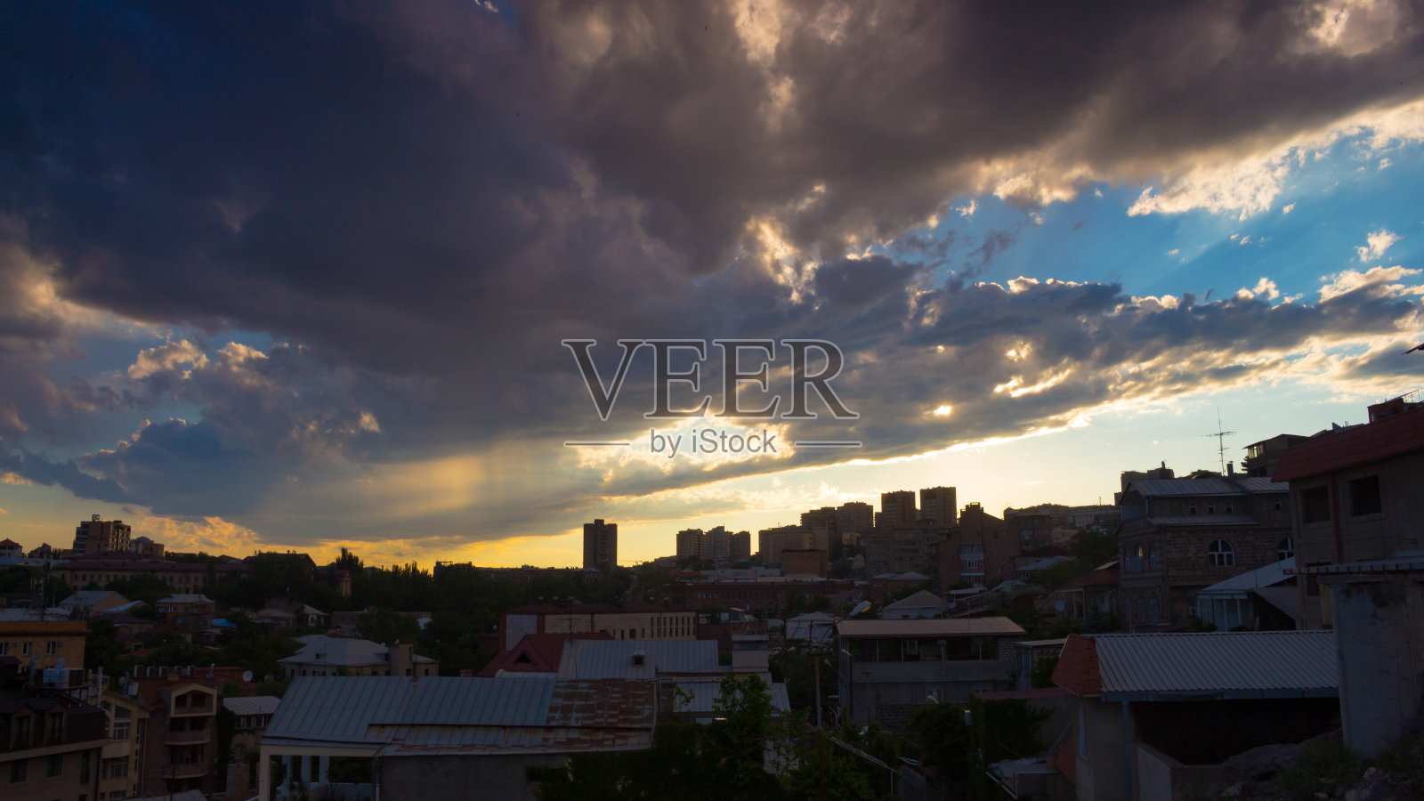 壮观的日落笼罩在城市的风景中，蓝天上有蓬松的云彩、雨水和金色的太阳。照片摄影图片