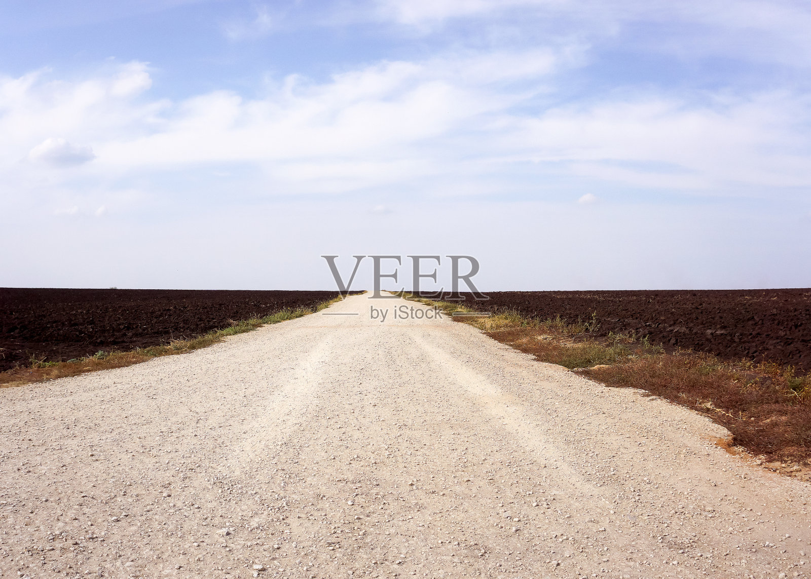 乡间小路上覆盖着浅灰色的土壤。这条路一直延伸到地平线。照片摄影图片