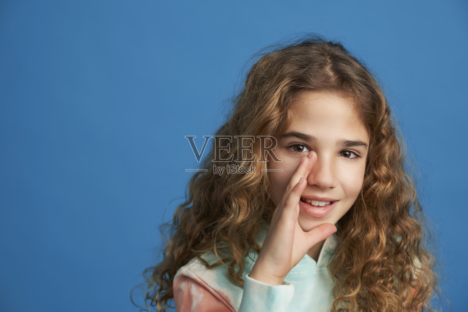 同情的女孩低语一个秘密的肖像与手近嘴孤立在蓝色背景。照片摄影图片