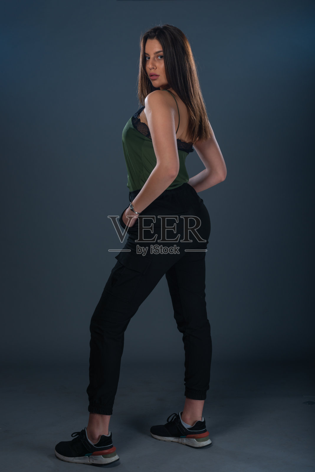 一名年轻女模特的肖像站在工作室里，穿着深绿色的上衣和黑色的裤子照片摄影图片