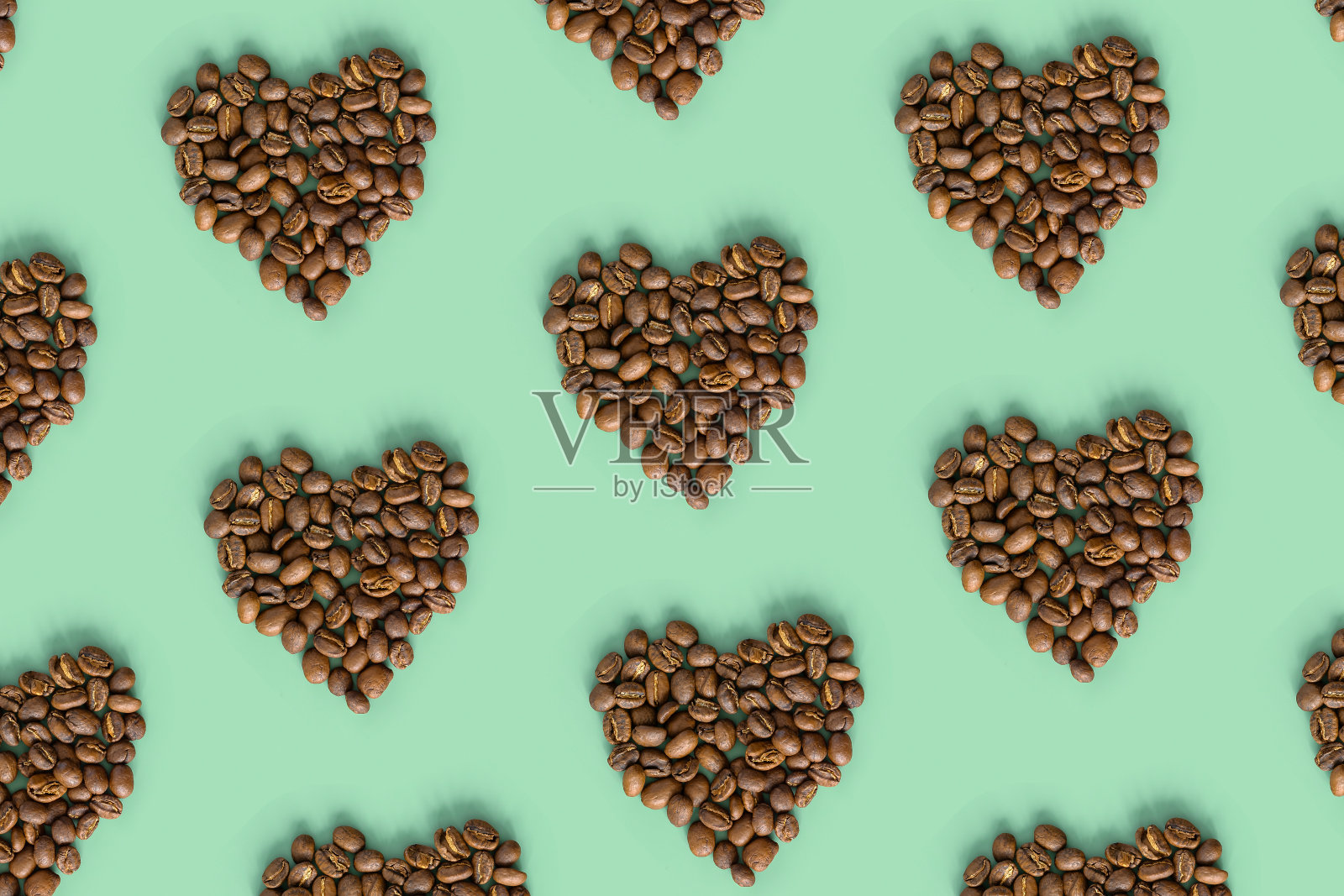 薄荷色背景上的咖啡豆形状心形，烤棕咖啡浆果，时尚的几何图案设计，俯视图，最小的平铺照片摄影图片