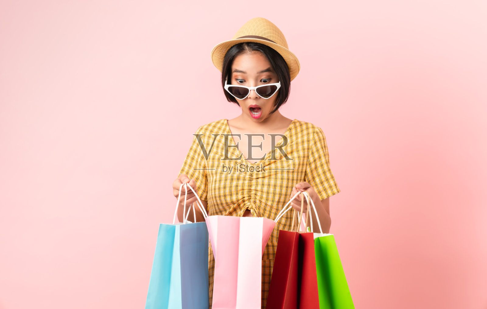 年轻微笑的亚洲妇女，拿着彩色购物袋，看着白色的背景。照片摄影图片