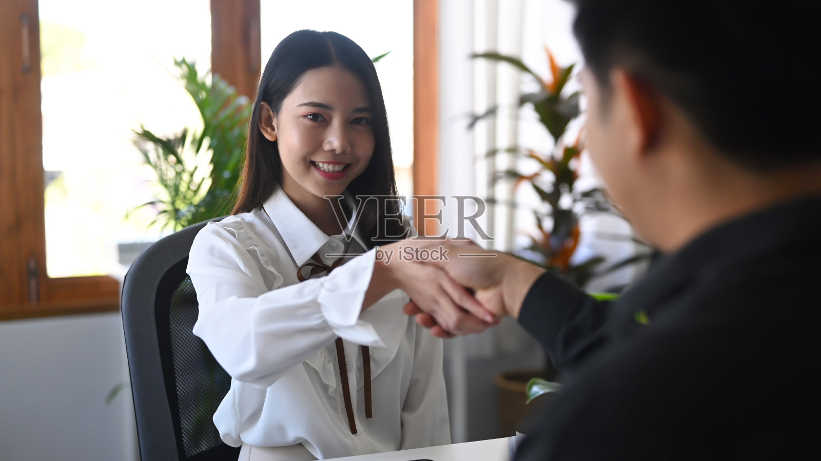 快乐的年轻女商人正在和她的生意伙伴握手。照片摄影图片