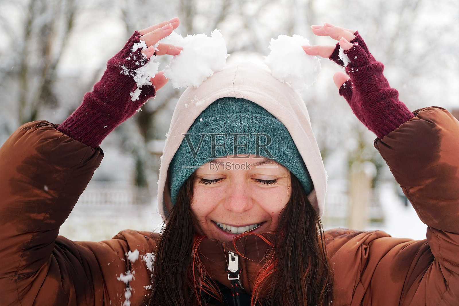 年轻女子在户外公园用雪球做兔子耳朵。微笑着享受冬天下雪的女人。一个女人在冬季森林的肖像。照片摄影图片