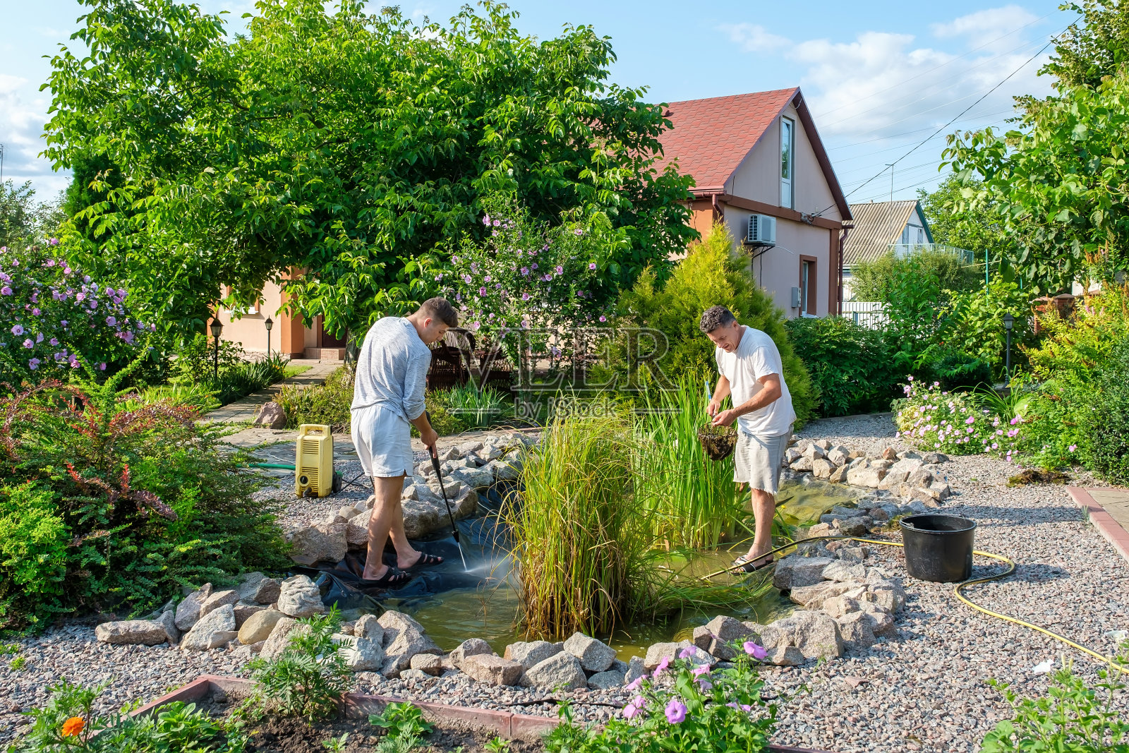 父子俩用高压清洗机清洗花园池塘底部的泥浆照片摄影图片