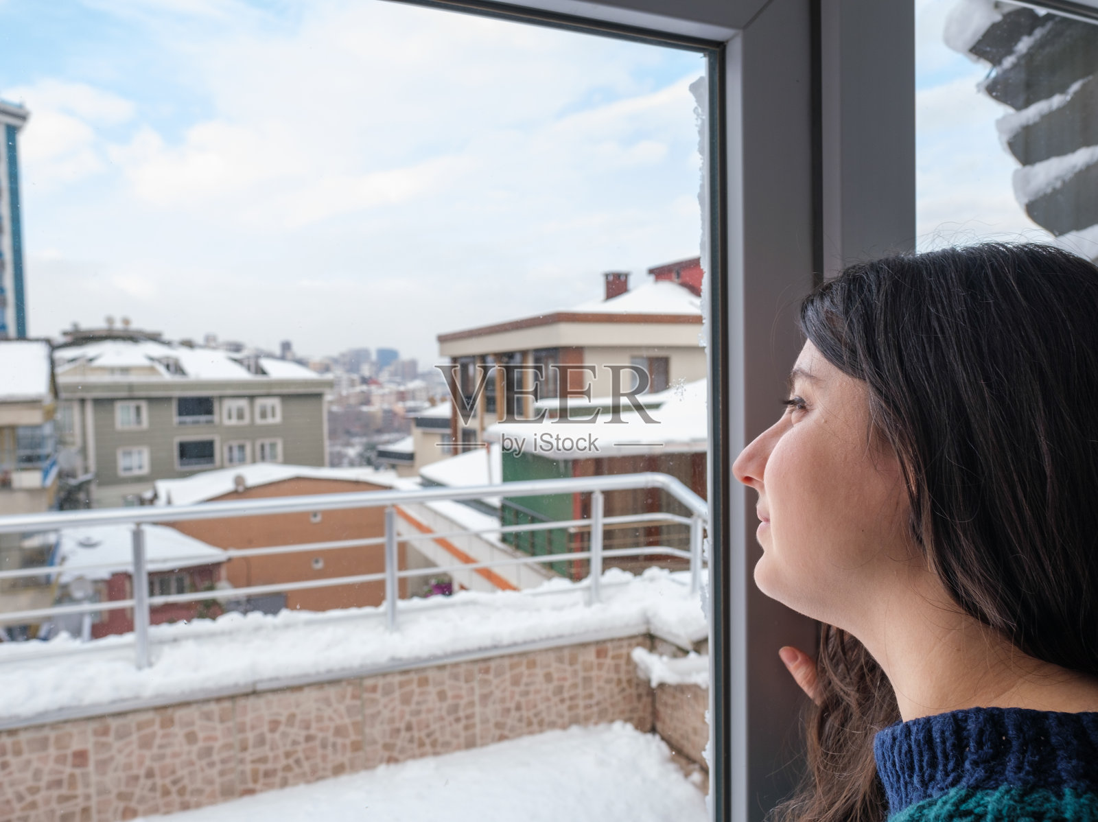 降雪后，年轻女子从窗户望向城市景观照片摄影图片