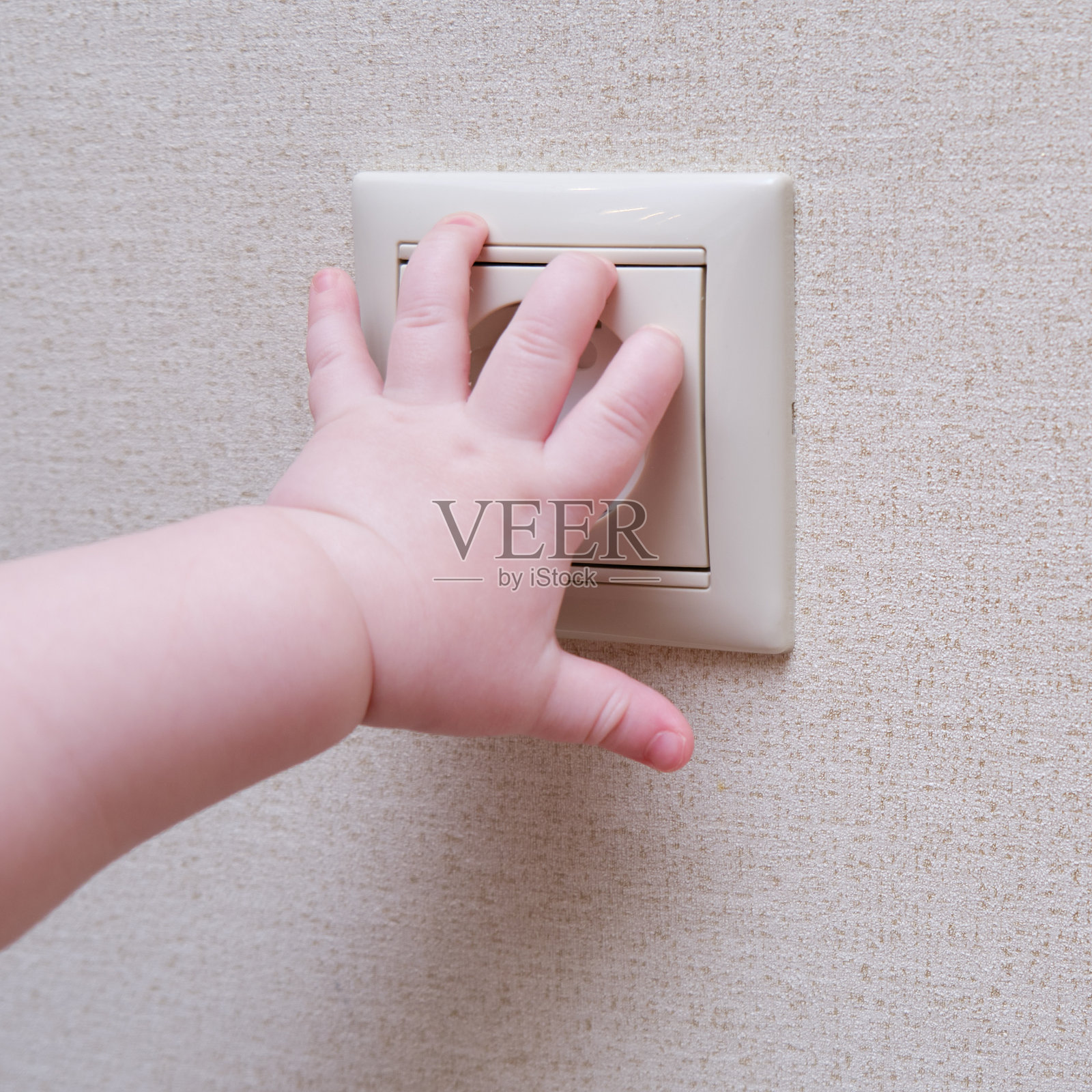 蹒跚学步的婴儿把手伸进家里墙上的插座里。儿童手指触电的危险及保护照片摄影图片