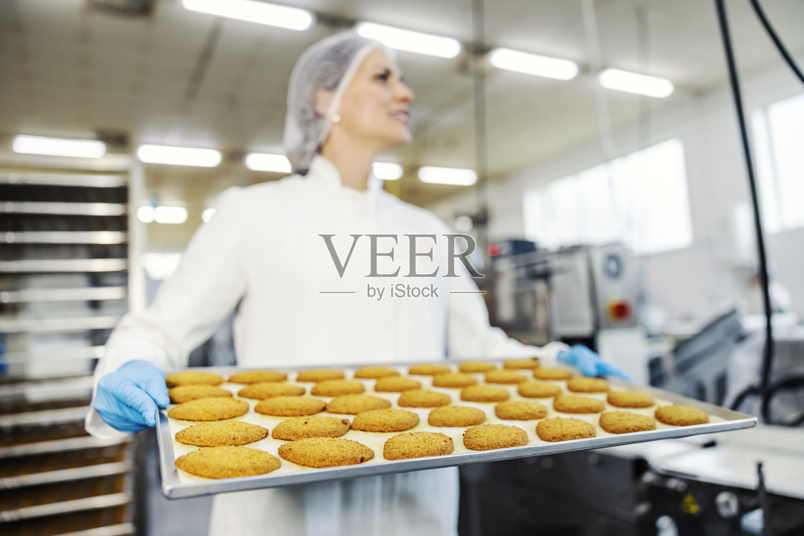 食品厂的工人端着装饼干的托盘。照片摄影图片