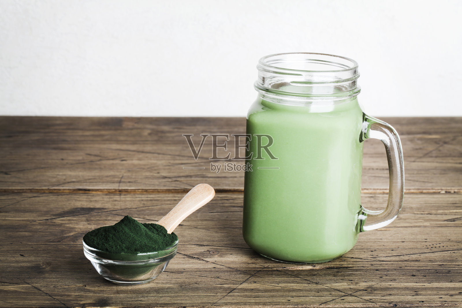 新鲜的绿色冰沙装在玻璃瓶和螺旋藻粉与勺子在木制背景。有用的习惯，自我照顾和健康的生活方式。本空间照片摄影图片