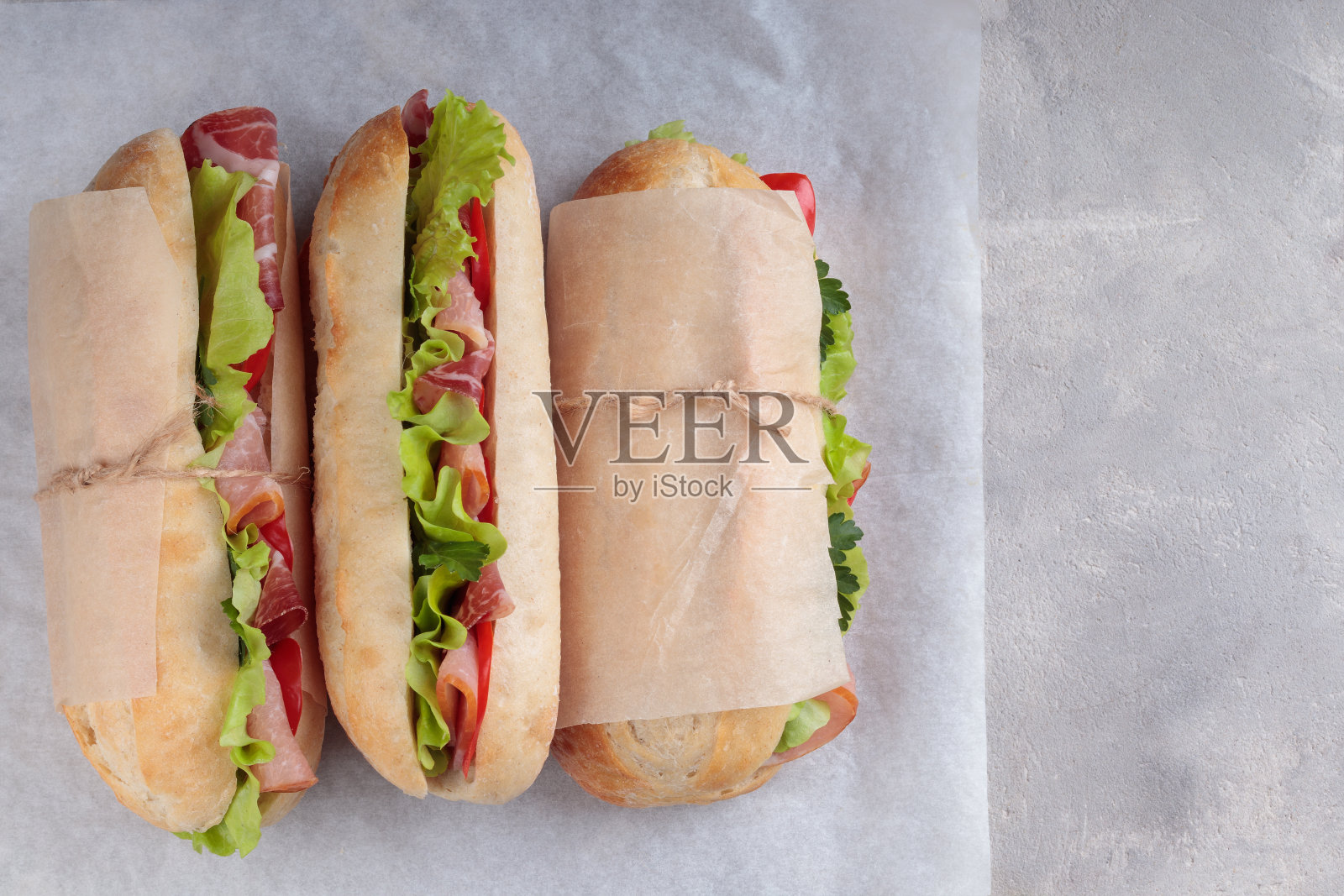 三份夹着烤猪肉片、辣椒和沙拉的banh mi三明治用白纸包好。照片摄影图片