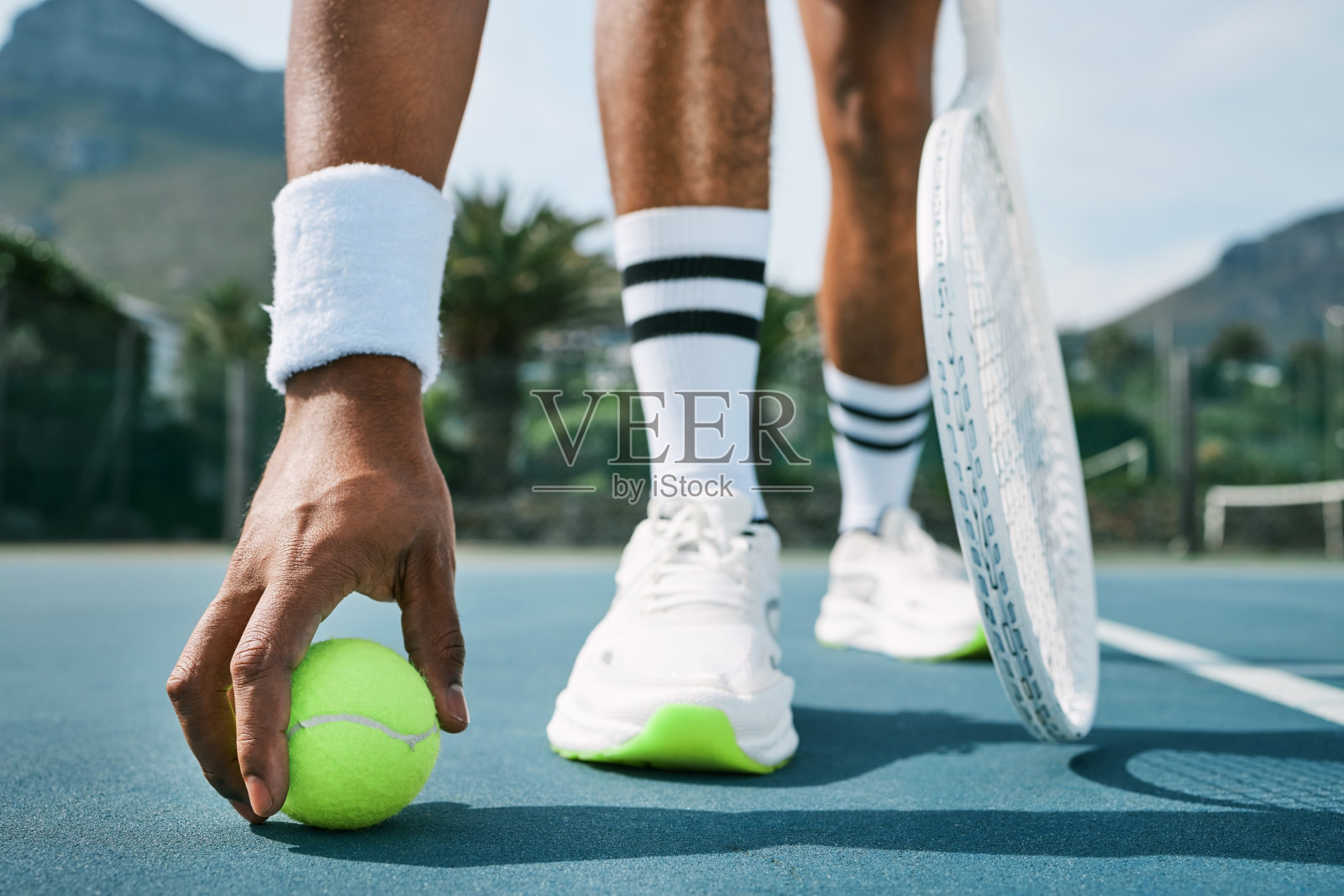 裁剪的镜头，一个不认识的人弯腰捡起一个网球练习照片摄影图片