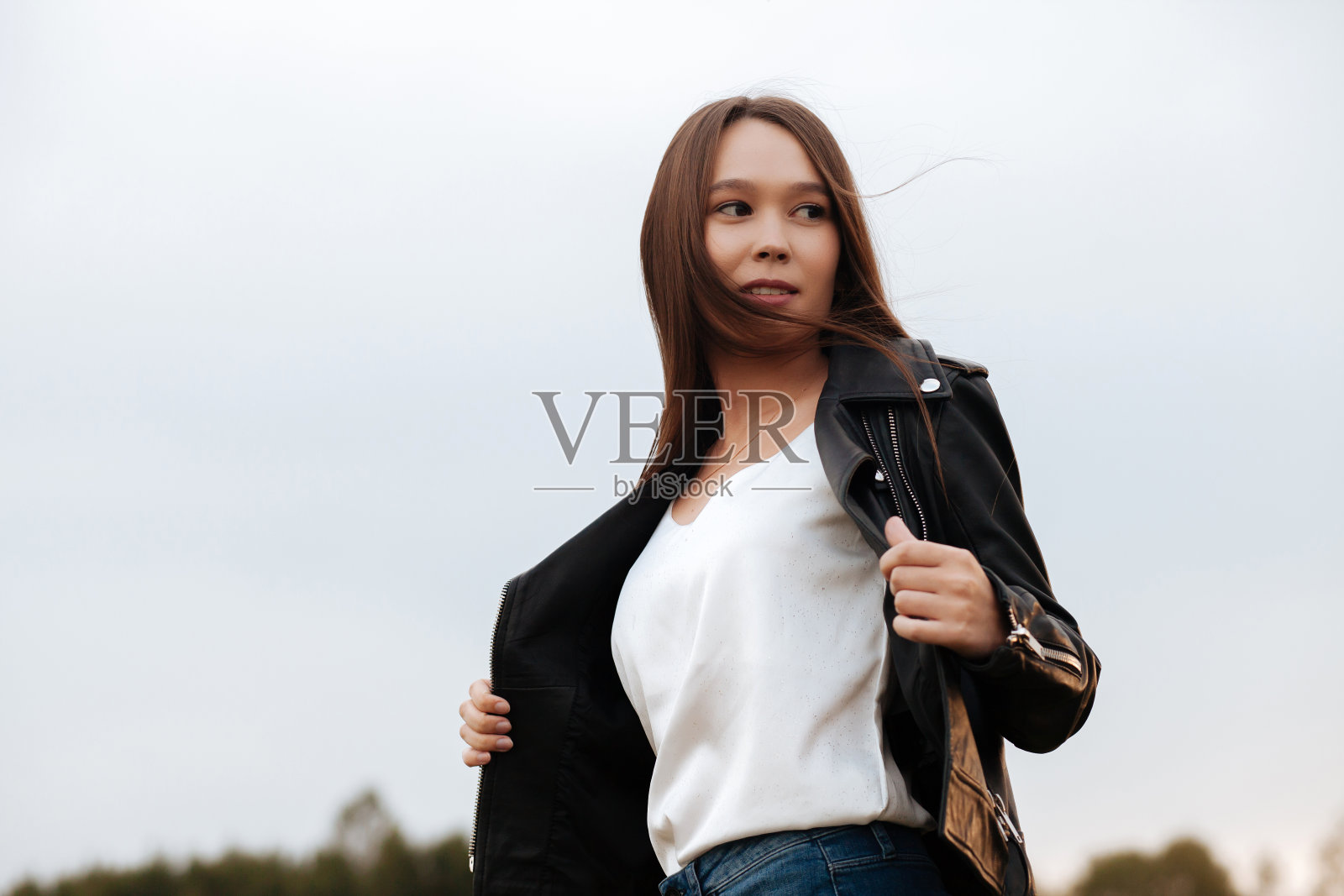 年轻的黑发女人穿着皮夹克和牛仔裤在大自然中照片摄影图片