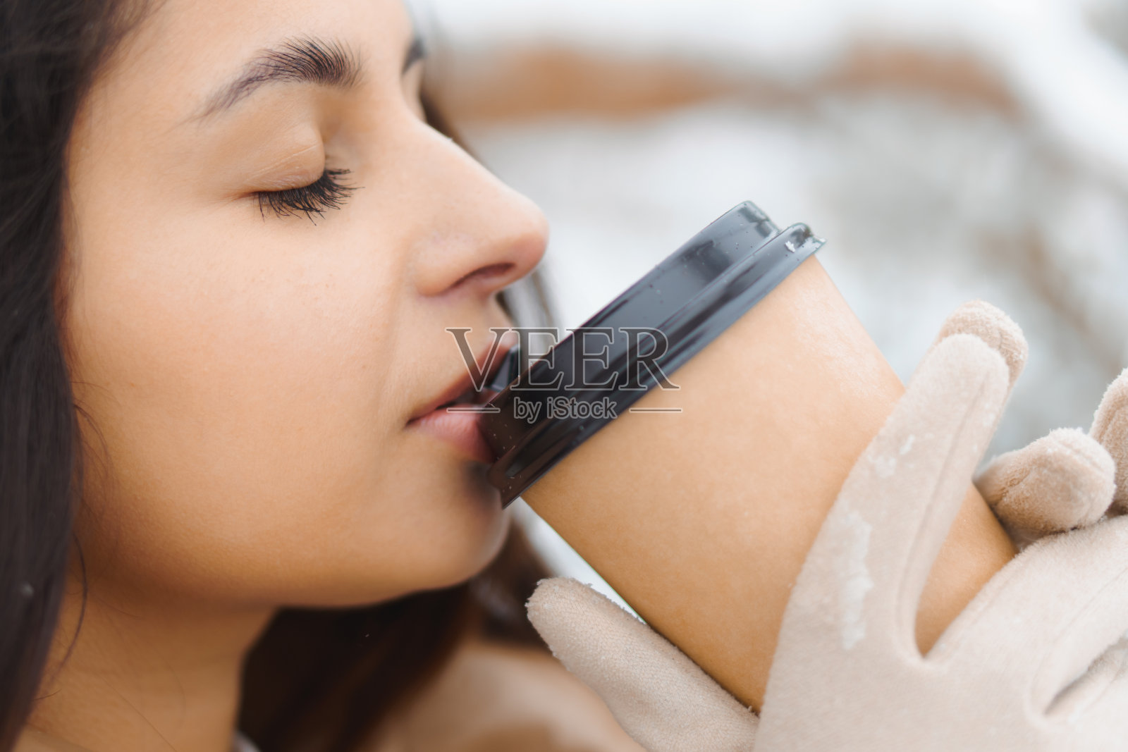 年轻可爱的黝黑黑发女人喝咖啡从纸杯在雪天的冬季森林照片摄影图片