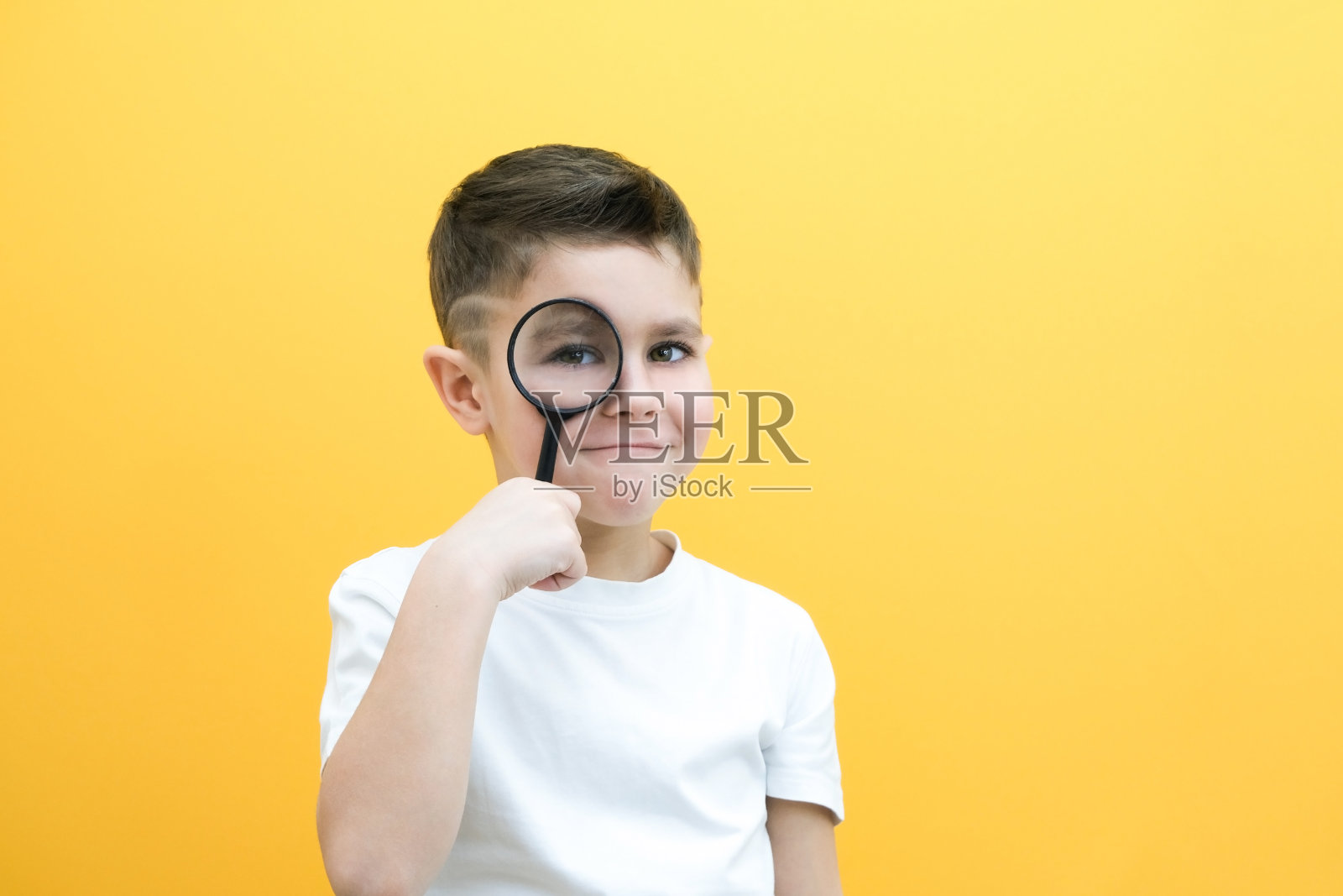 一名好奇的男生穿着便服，正透过放大镜看相机照片摄影图片