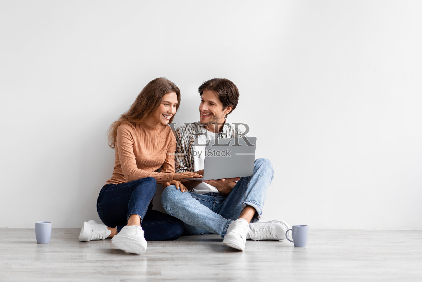 满意的年轻白种人夫妇看着笔记本电脑规划新的内饰，坐在空房间的地板上照片摄影图片