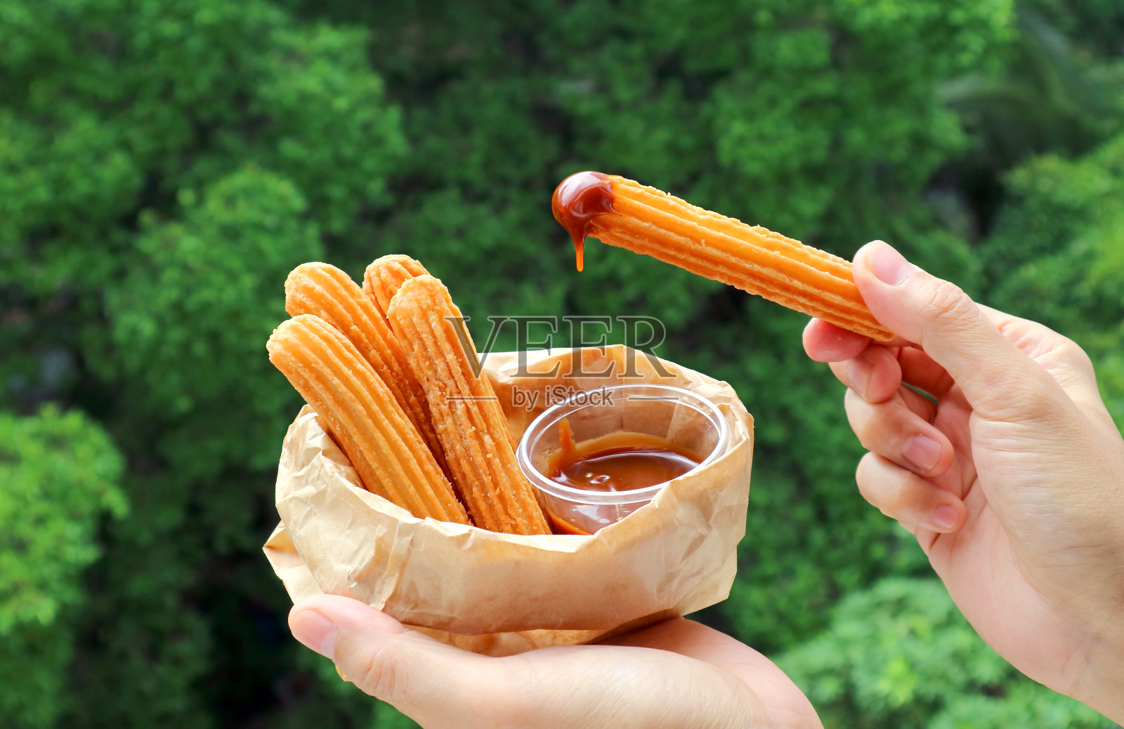 手蘸新鲜油炸油条在牛奶或焦糖酱照片摄影图片