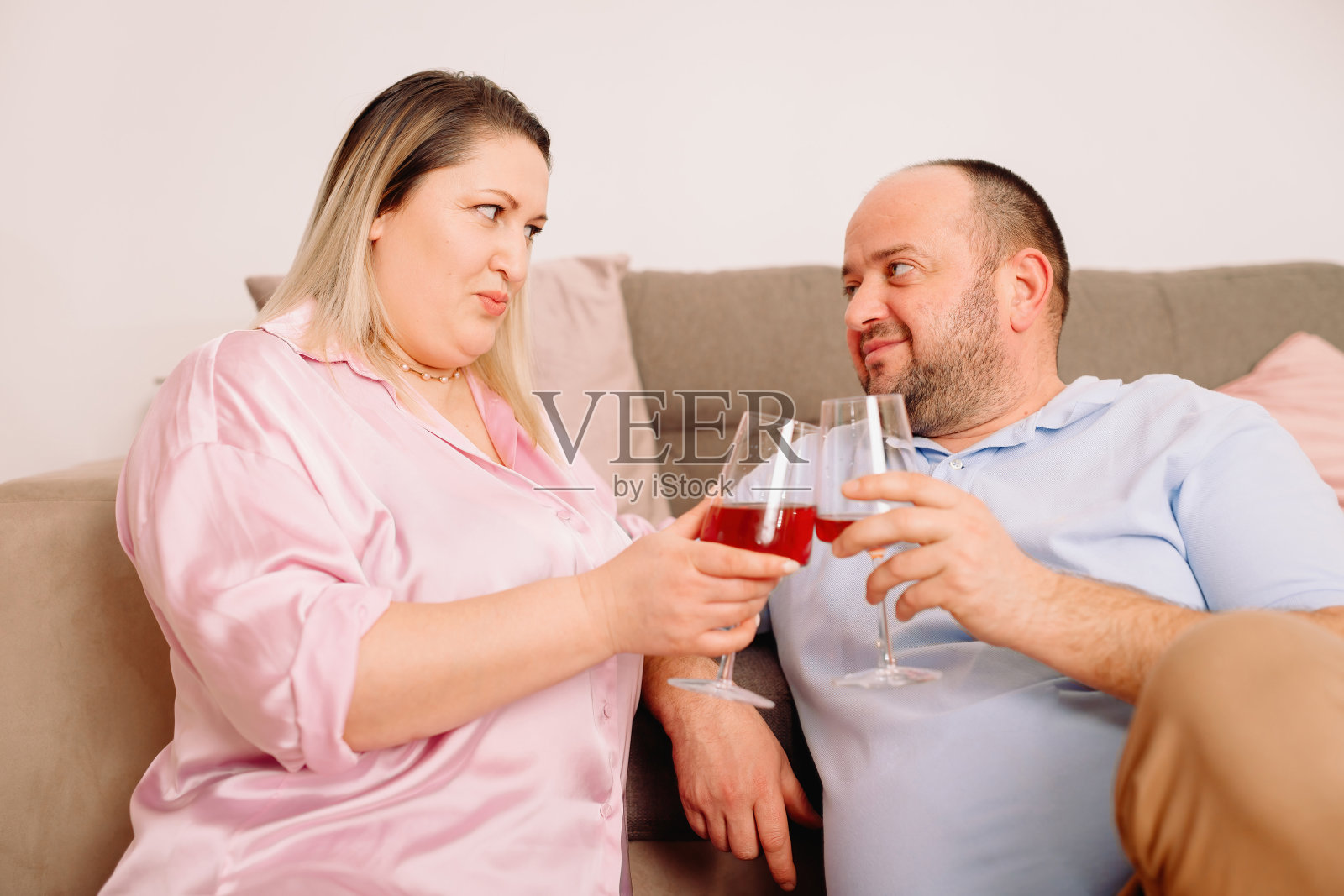 幸福的白种人夫妇在家里舒适的沙发上休息，手里拿着两杯葡萄酒，用爱看着对方。照片摄影图片