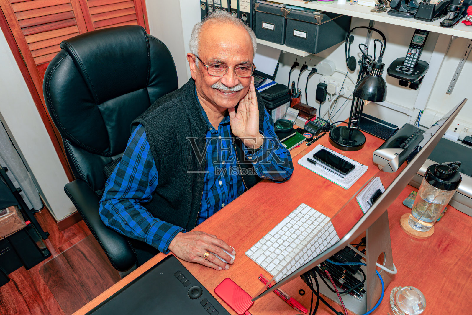 Bogotá，哥伦比亚-一个白发苍苍，74岁的亚洲印度人在他的家庭办公室在他的桌面电脑上工作。他的行为似乎在说，“现在看起来不错。”照片摄影图片