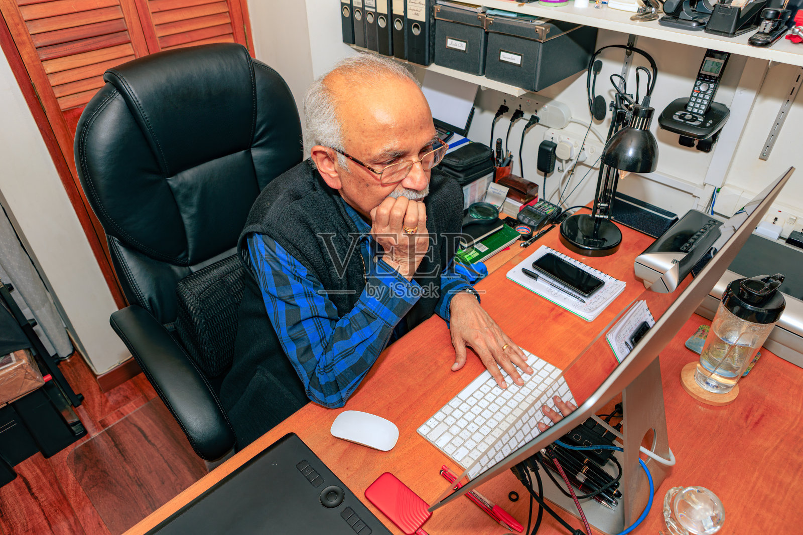 Bogotá，哥伦比亚——一位白发苍苍、74岁的亚洲印度人在他的家庭办公室的桌面电脑上工作，似乎有点担心他在电脑屏幕上看到的东西。照片摄影图片