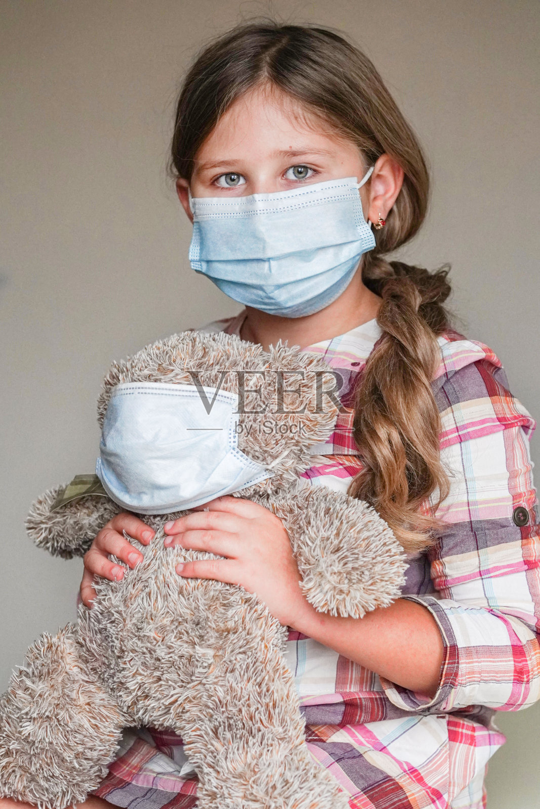 小女孩抱着玩具泰迪熊，戴着医用防护口罩。冠状病毒Covid-19大流行期间的儿童保护概念。疫苗接种、医疗保健的概念。照片摄影图片