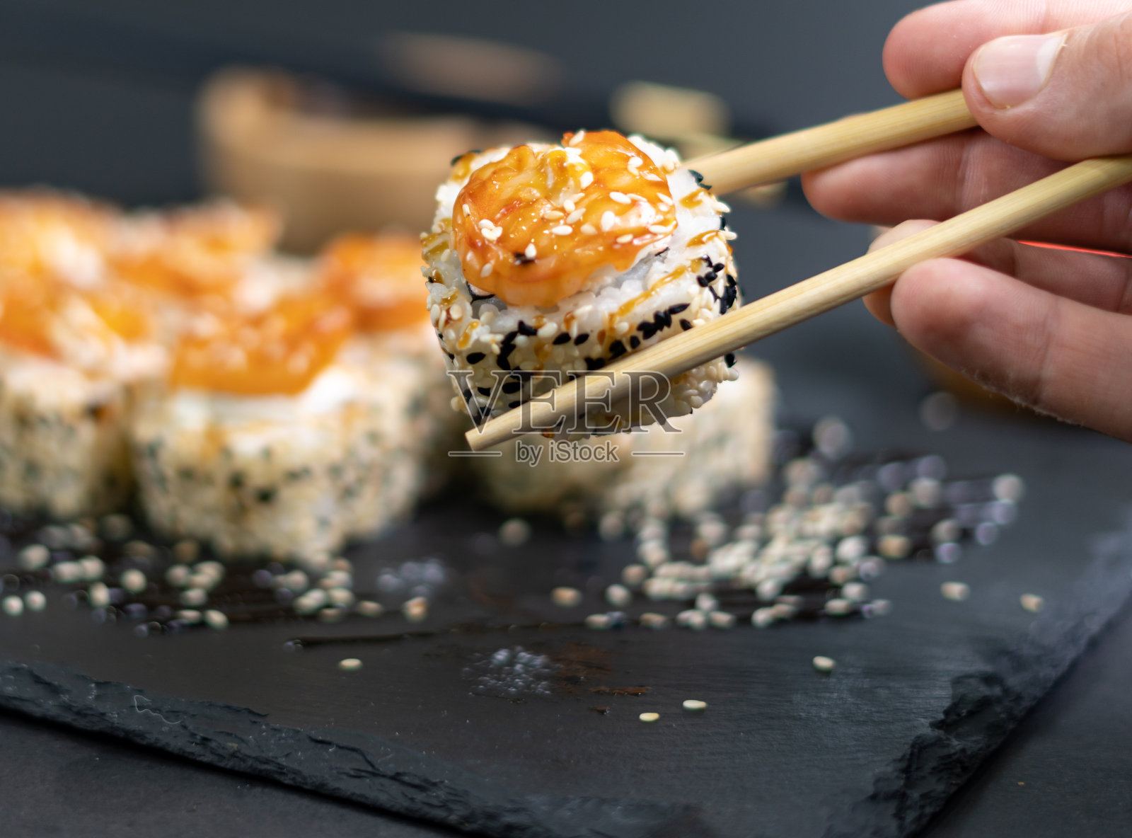 用竹筷夹住的虾寿司的特写。黑底芝麻虾寿司。日本寿司照片摄影图片