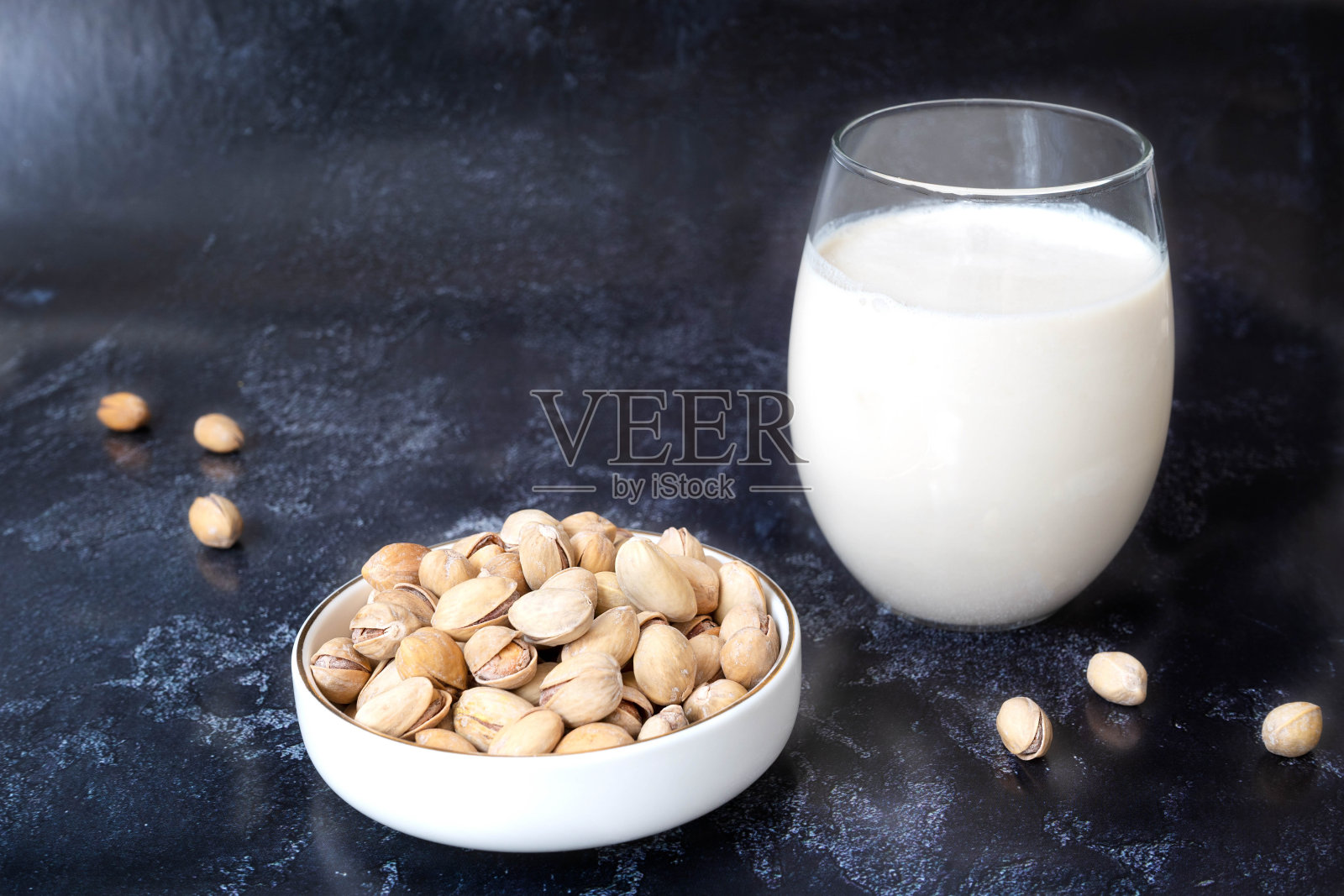 一个透明的玻璃与开心果牛奶站在黑暗的背景。旁边是一碗白色的开心果。理念天然有机产品，素食食品。特写镜头照片摄影图片