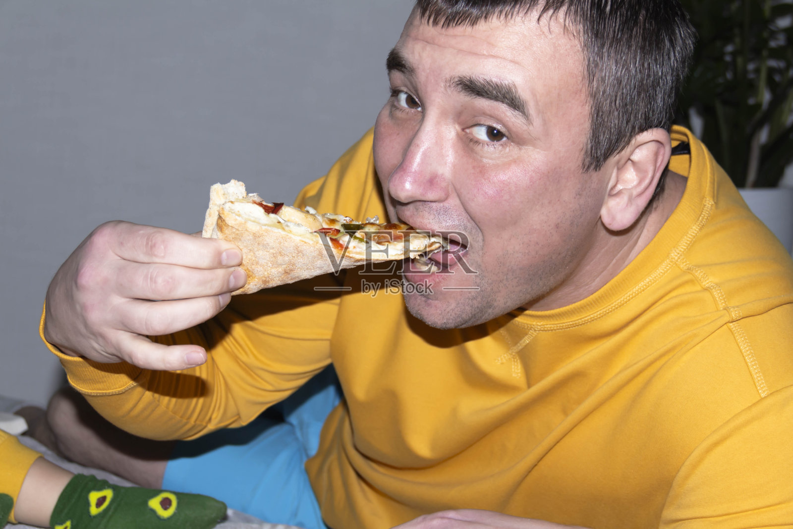 一个穿着黄色夹克的男人吃着美味而芬芳的披萨。照片摄影图片