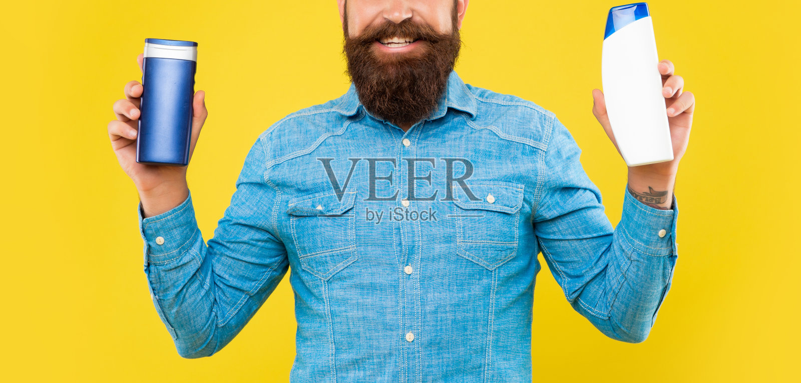 裁剪快乐野蛮的大胡子男人在黄色背景上选择洗发水瓶子，展示洗漱用品照片摄影图片