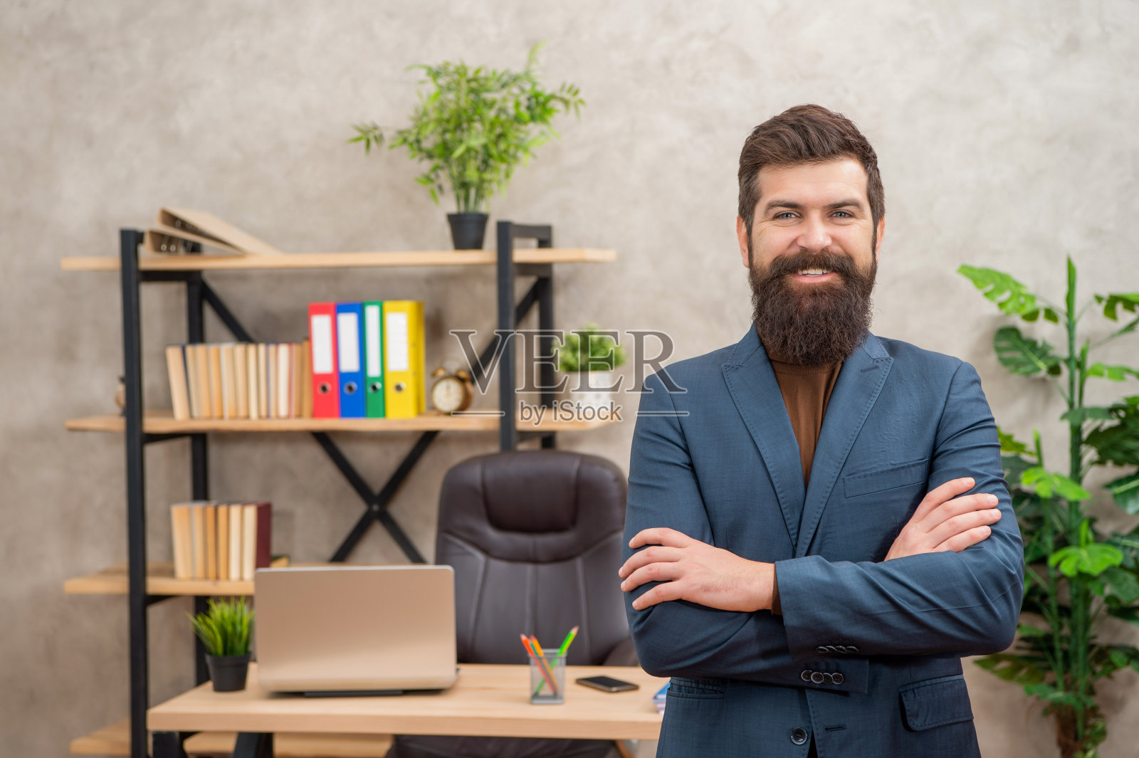 快乐的成熟企业家穿着夹克站在办公室里，穿着正装照片摄影图片