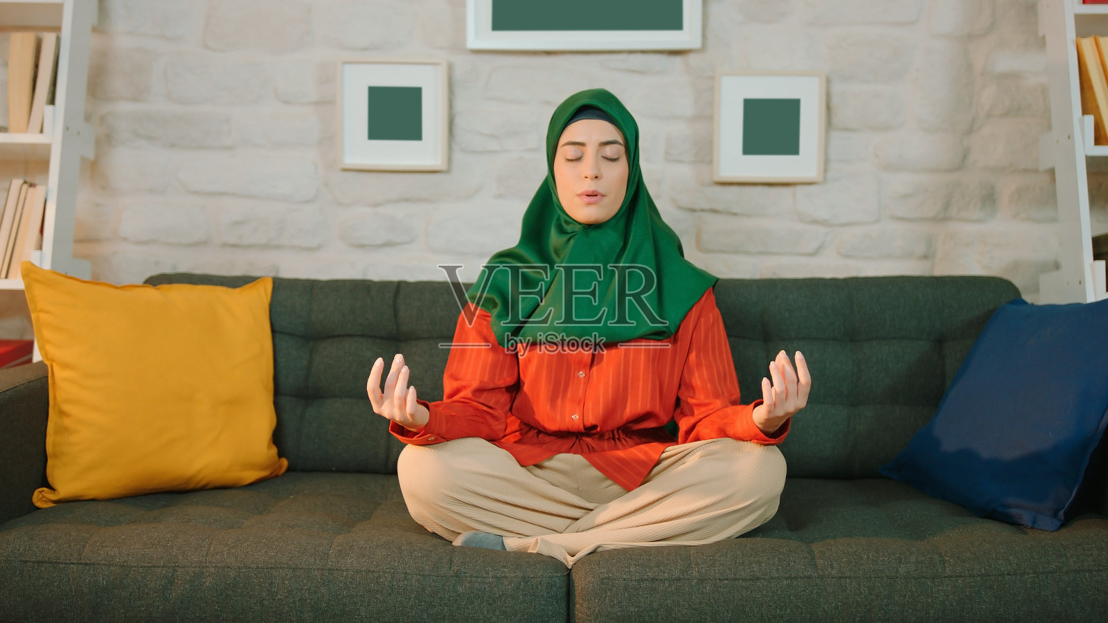 穆斯林妇女戴着头巾在家练习瑜伽。冥想。照片摄影图片