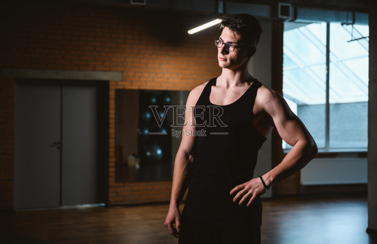 英俊友好的运动员或私人教练在健身房。年轻的运动男子微笑站在健身俱乐部的背景照片摄影图片