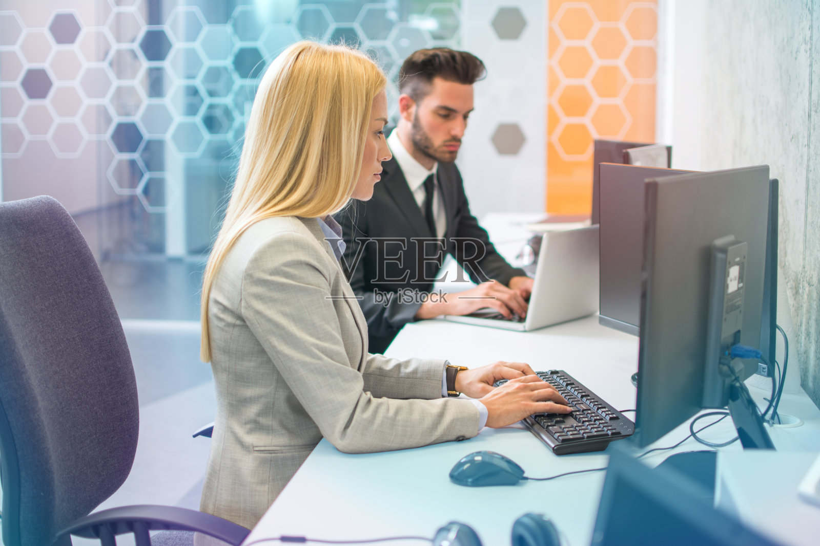 侧视图肖像有吸引力的金发女人穿着商业西装使用计算机在现代办公室。照片摄影图片