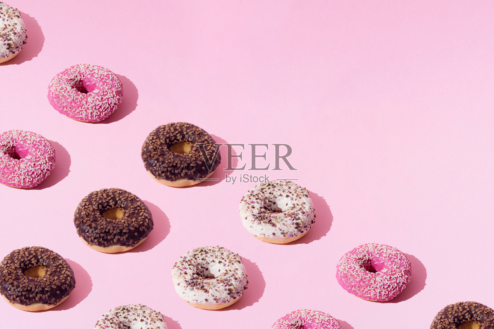 白色、粉色和巧克力色的环形甜甜圈。粉红色粉彩背景上的彩色碎屑。模式。照片摄影图片