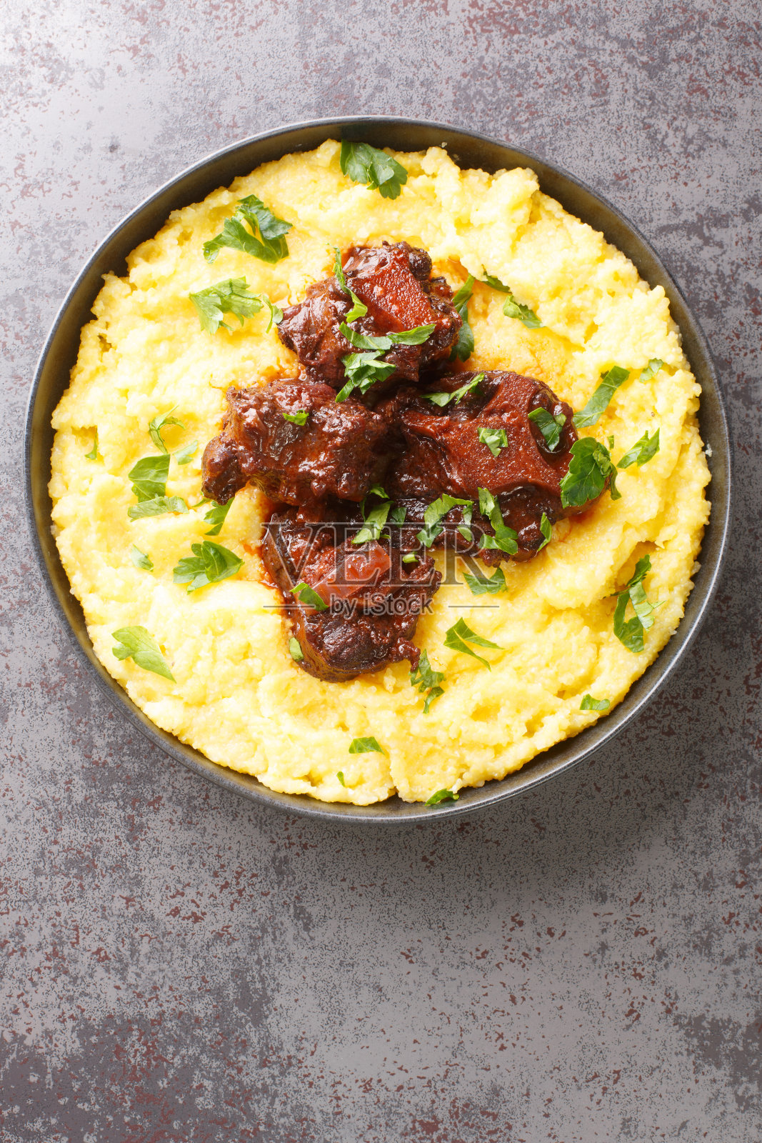 巴西传统食物炖牛尾拉巴达与玉米玉米粥特写盘。垂直的俯视图照片摄影图片