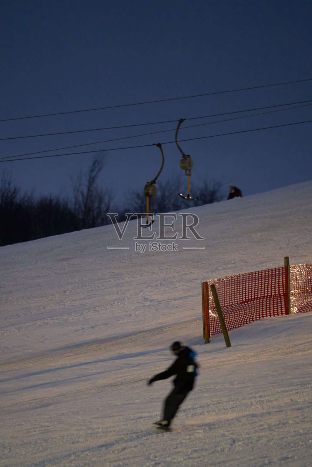 夜间有照明的滑雪牵引升降机在运行。冬季运动员在雪坡上。滑雪运动模糊。照片摄影图片