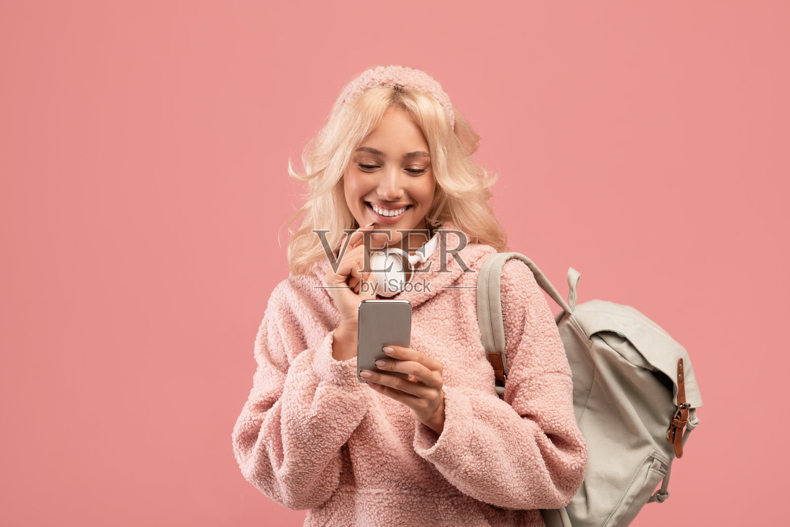 快乐的女学生使用智能手机，网络和短信，而站在粉红色的背景背包照片摄影图片
