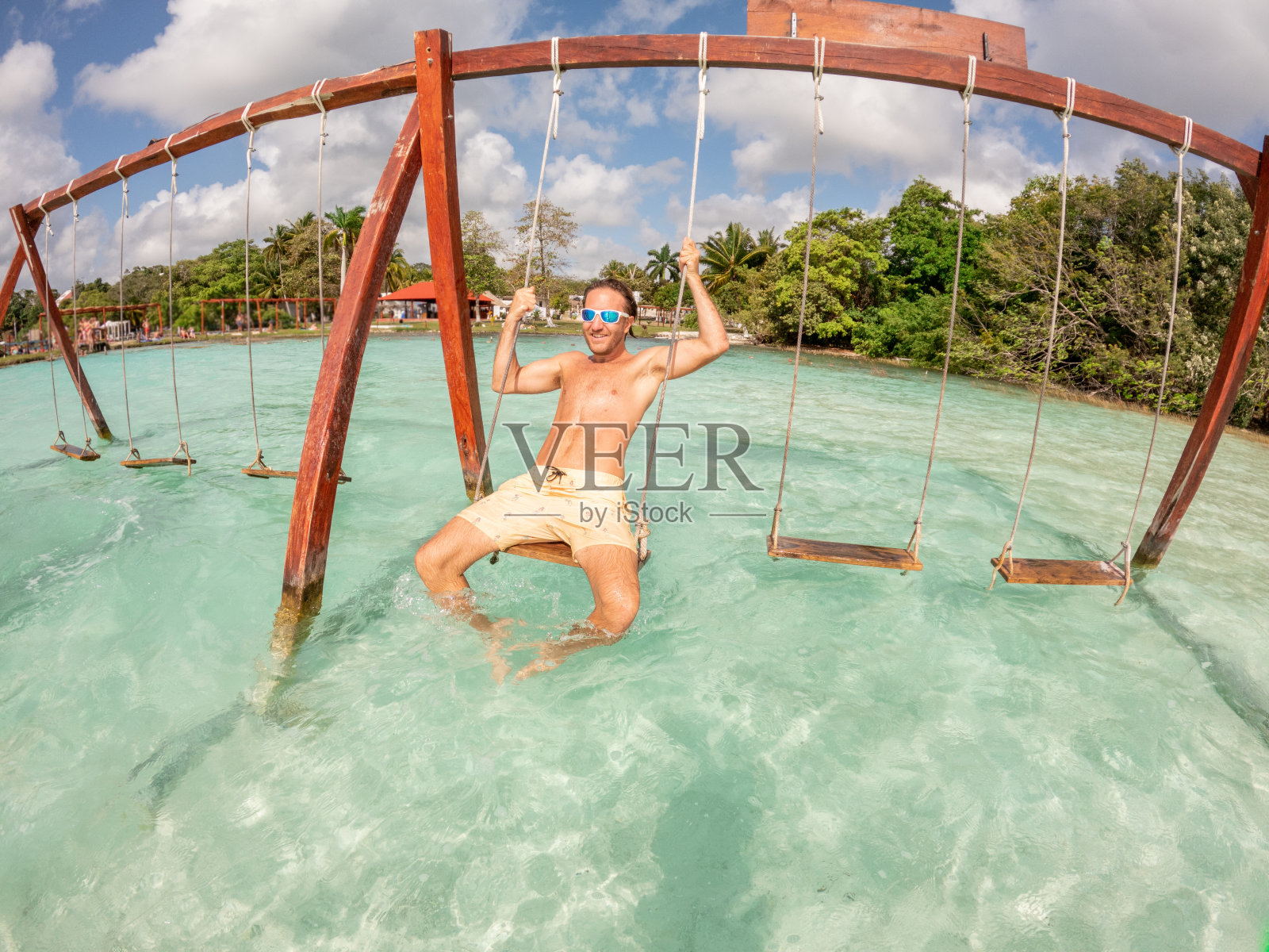 阳光明媚的一天，一个年轻人在美丽的泻湖上荡秋千玩得很开心照片摄影图片