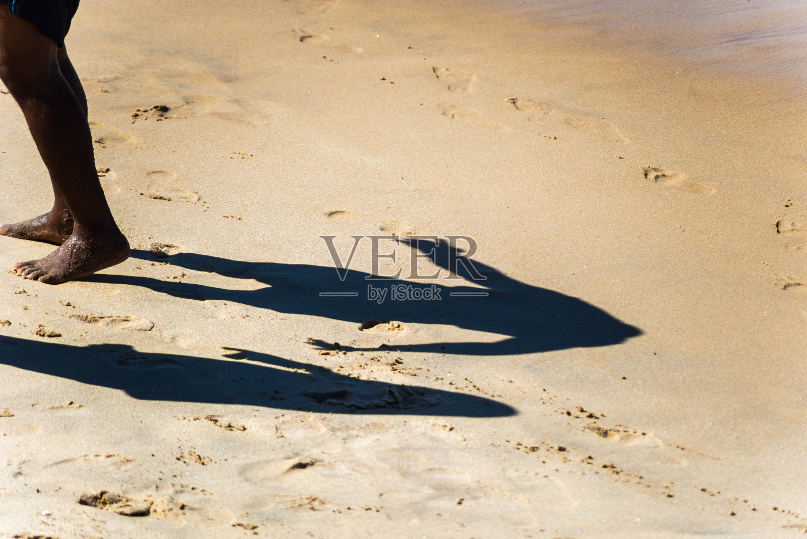 一个人的下部和他的影子在沙滩上。照片摄影图片