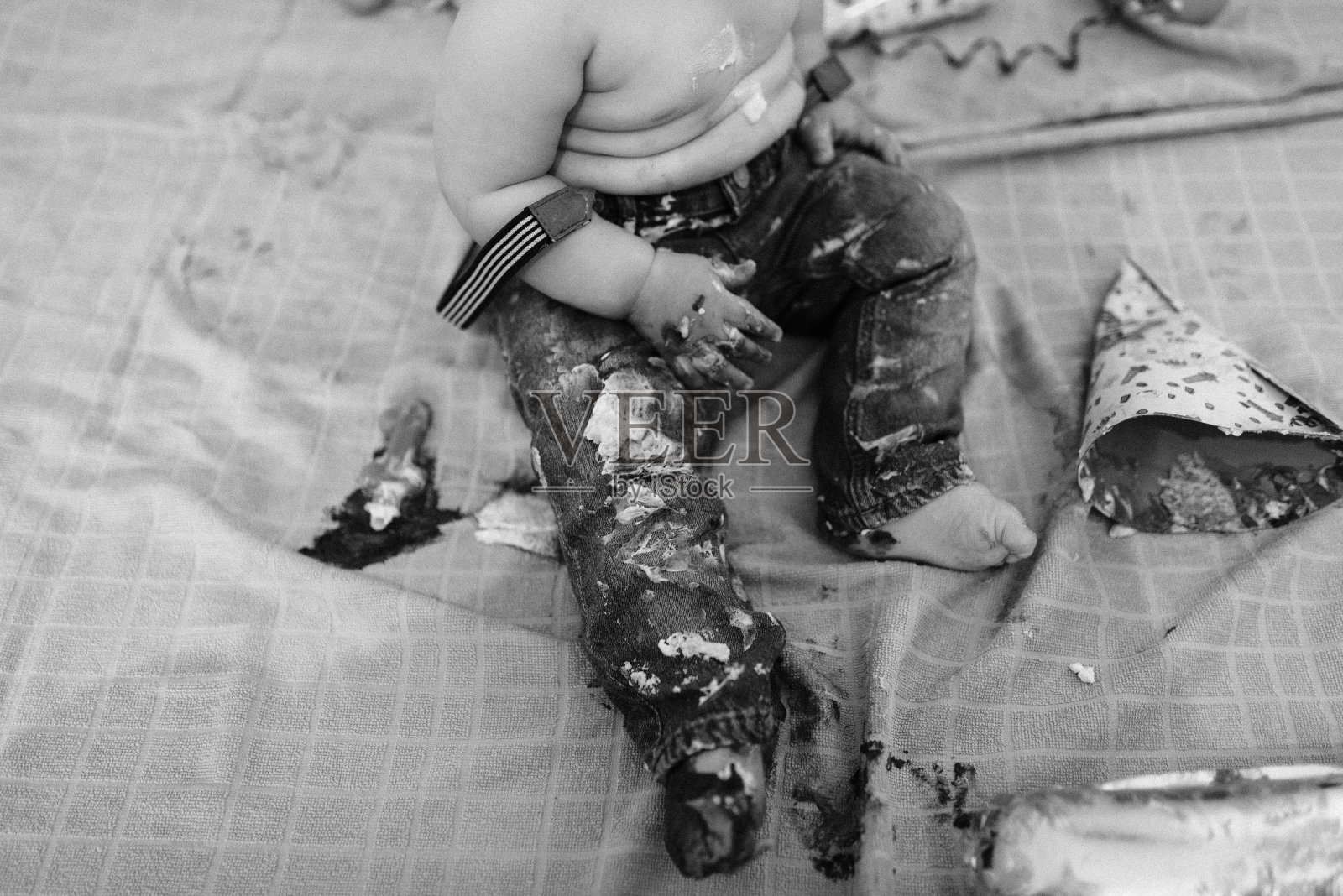 一个蹒跚学步的孩子的脚涂上了奶油，还有一个盘子里的蛋糕。照片摄影图片