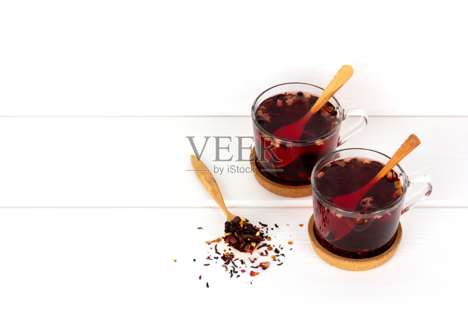 两杯浆果和花茶，木勺放在软木架子上，一个木勺放干茶在白色桌子上复印空间照片摄影图片