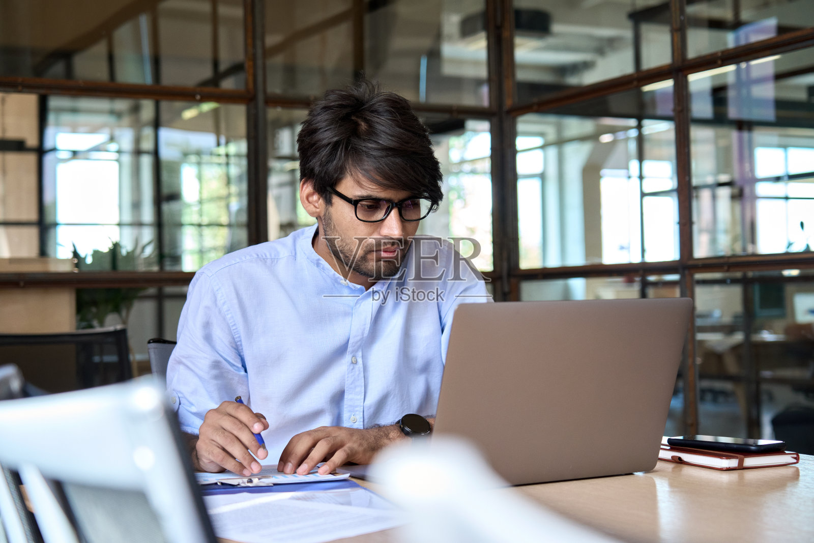 在办公室用笔记本电脑观看网络研讨会的年轻印度商人照片摄影图片