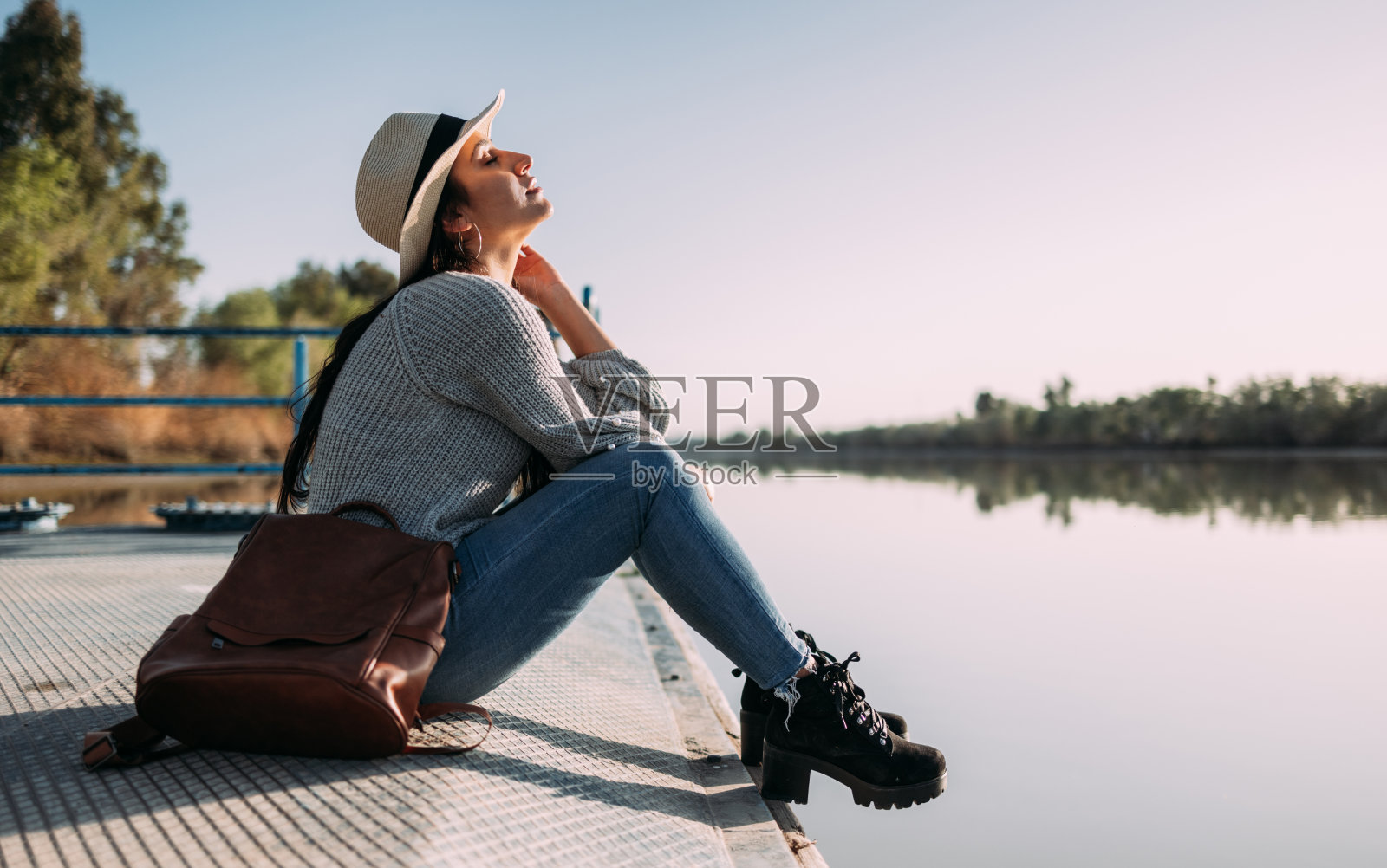 戴着帽子的拉丁女子在湖边的码头边休息照片摄影图片