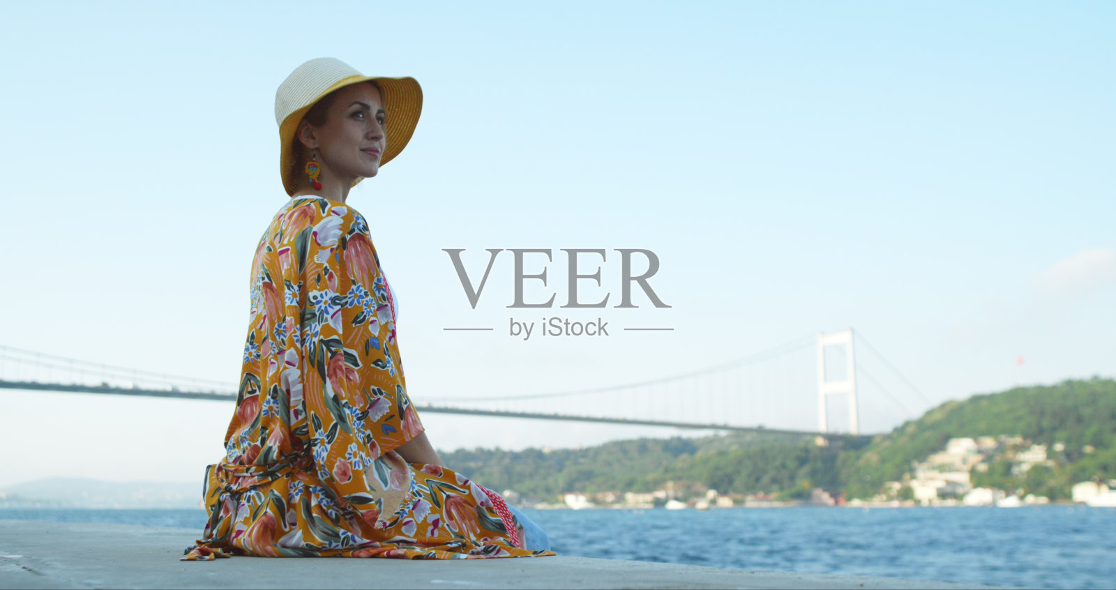 美丽迷人的年轻女孩戴着帽子，看着土耳其的博斯普鲁斯海峡。照片摄影图片