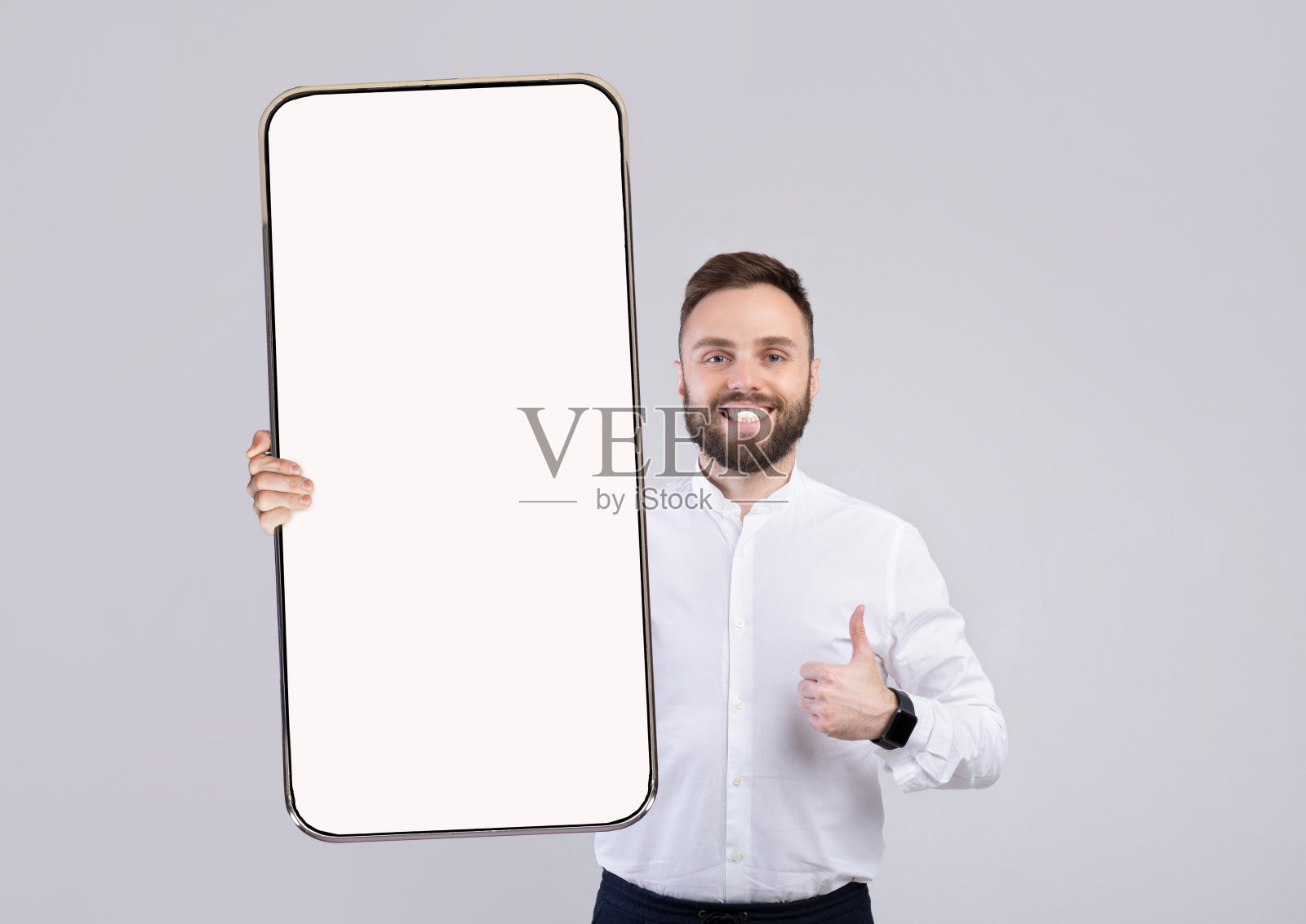 年轻快乐的男子拿着智能手机，屏幕是空白的，大拇指朝上照片摄影图片