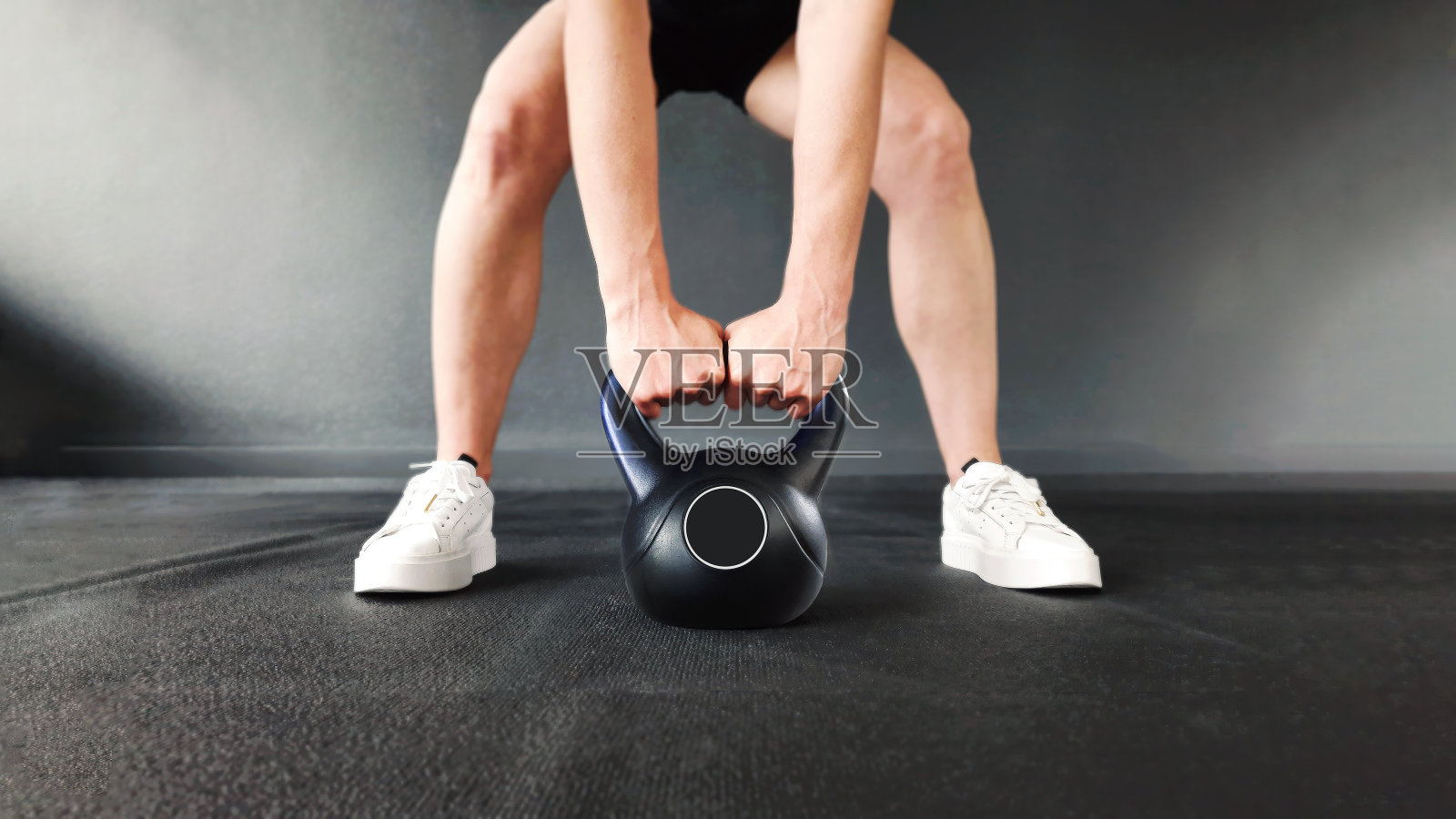 女性力量训练。这个女孩用壶铃展示了二头肌和三头肌的健身练习。以健身俱乐部的黑色墙壁为背景，在健身房里训练。为广告制作健身横幅。照片摄影图片