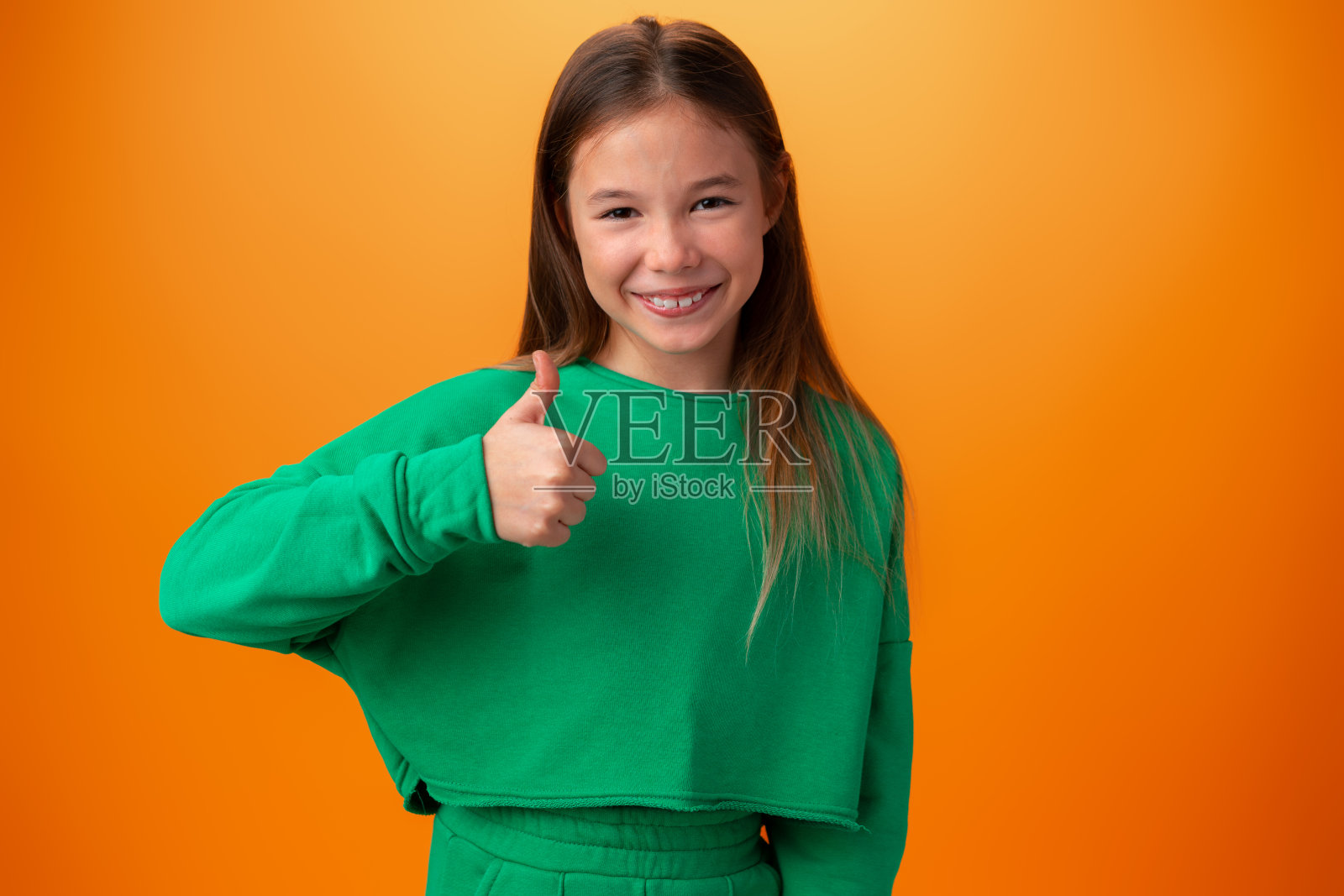 在橙色背景前竖起大拇指的少女照片摄影图片