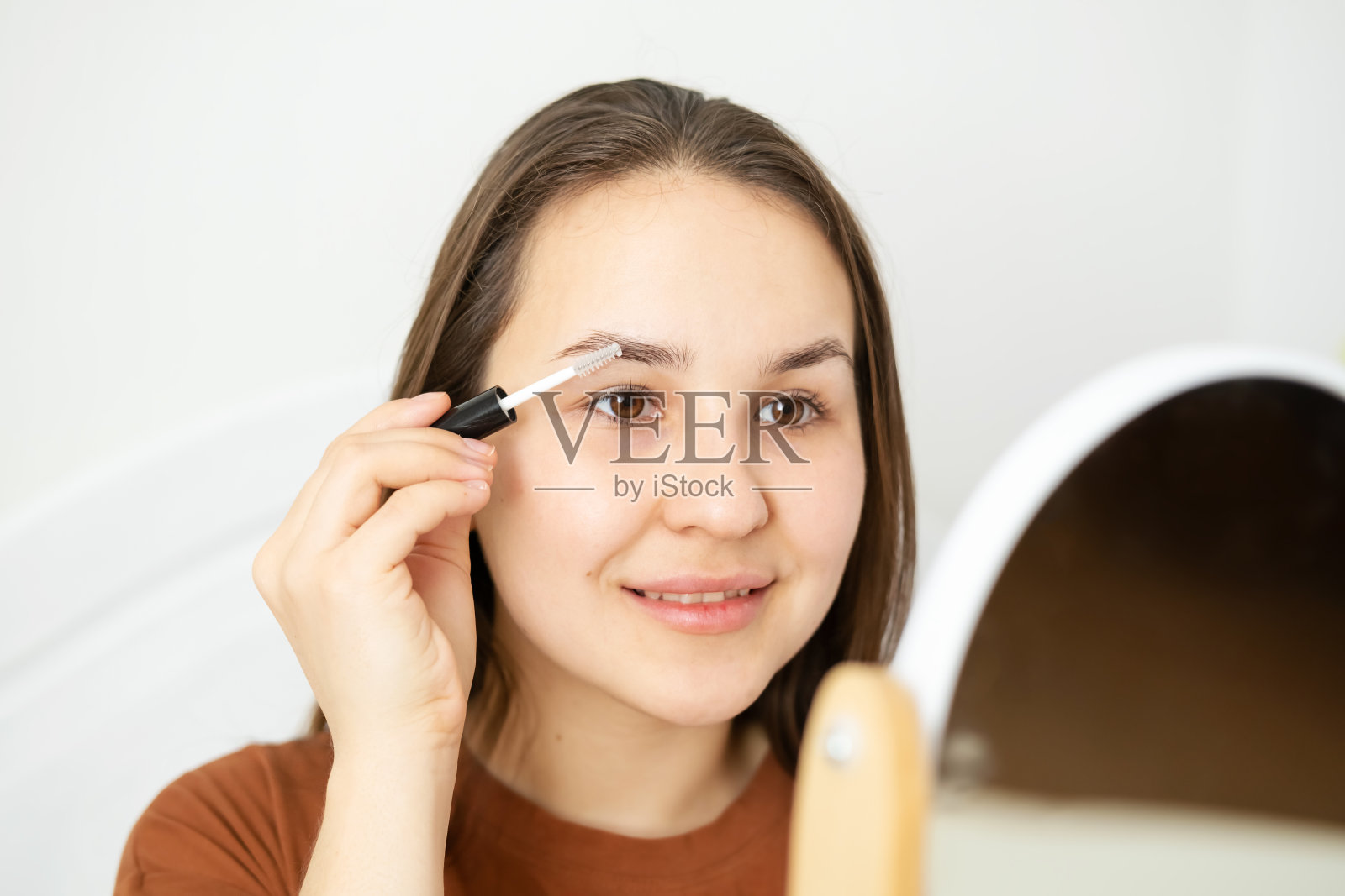 近距离的肖像年轻美丽的女人，女孩坐在家里打赌，看着镜子和画他的眉毛。早上的面部护理和化妆应用。照片摄影图片