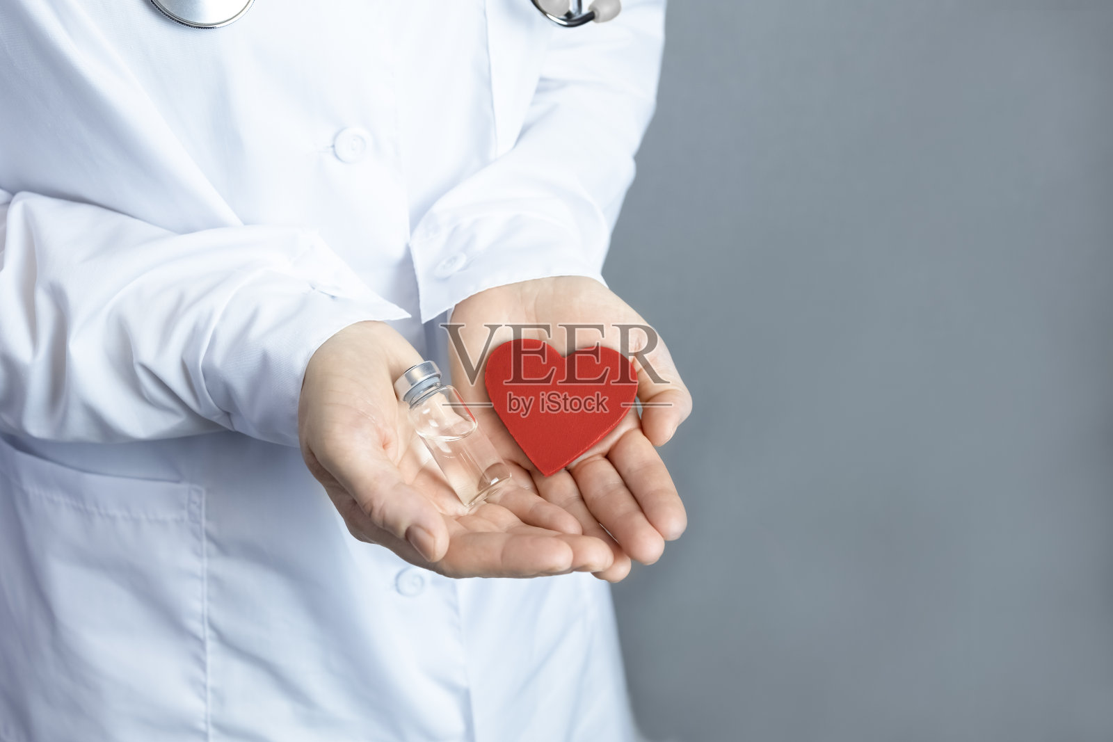 医生手里拿着一颗红心和一个装有透明液体(药物、疫苗)的安瓿。照片摄影图片