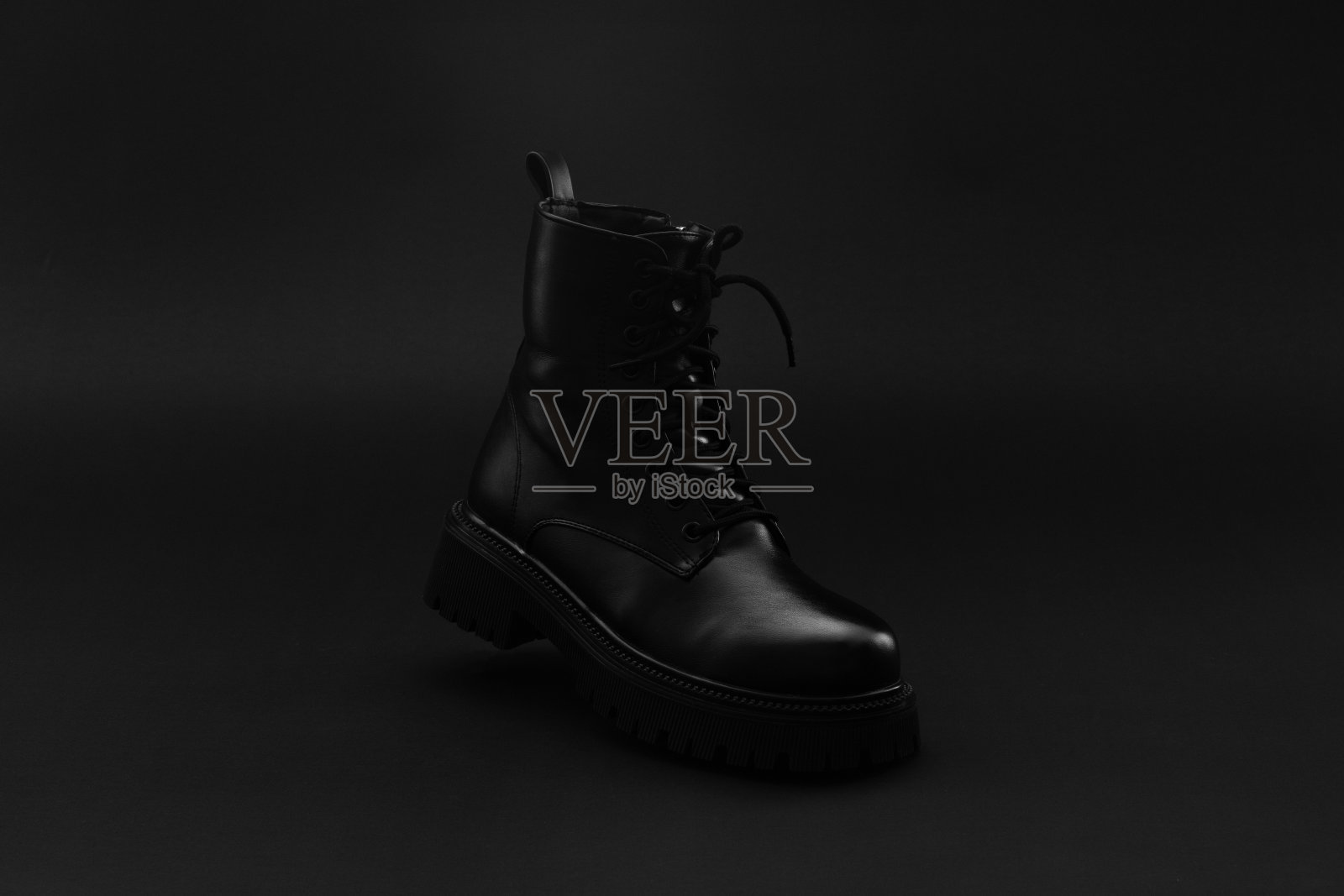 一个孤立的黑色皮革秋冬中性靴子站在明亮的黑色背景。粗跟，圆趾，压纹硬底的靴子。本空间照片摄影图片