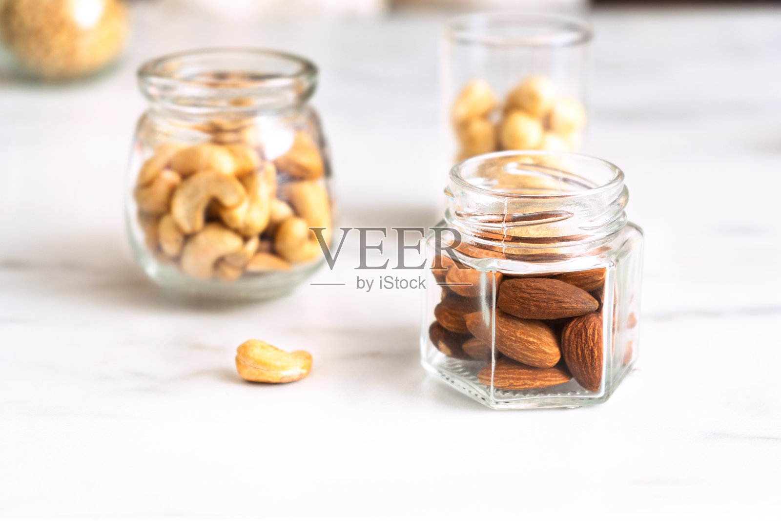白色的桌子上放着三个玻璃罐，里面装着不同的去皮坚果(杏仁、腰果、榛子)。各种新鲜的烤坚果。天然有机产品理念。健康食品,零食。照片摄影图片